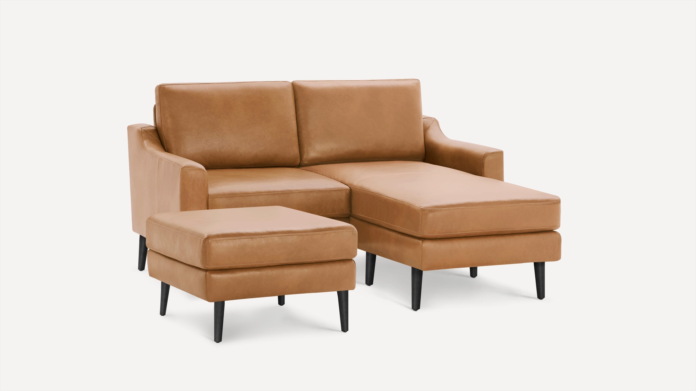 Modern tan leather sectional sofa with chaise lounge and matching ottoman, featuring black tapered legs and clean lines.