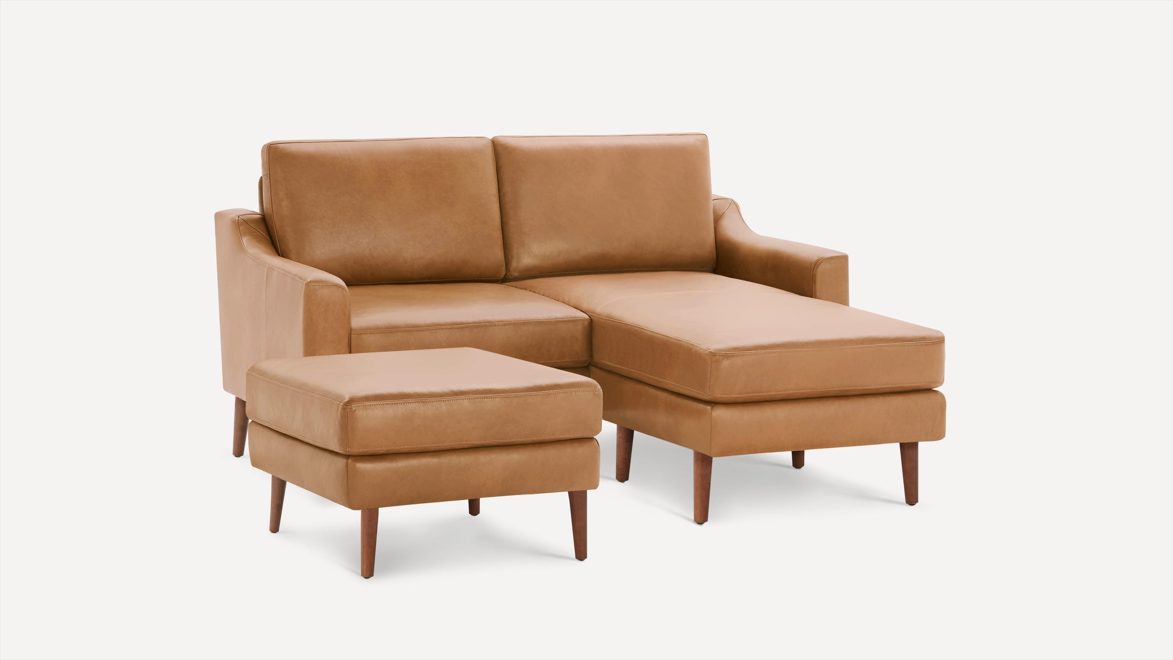 Mid-century modern tan leather sectional sofa with wooden legs and matching ottoman on white background.