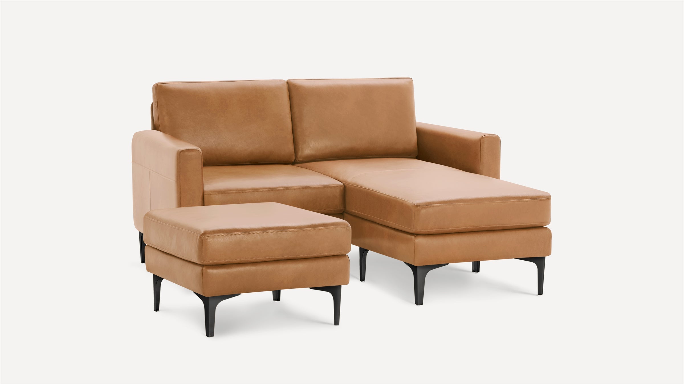 Modern tan leather sectional sofa with chaise lounge and matching ottoman on black legs, set against a white background.