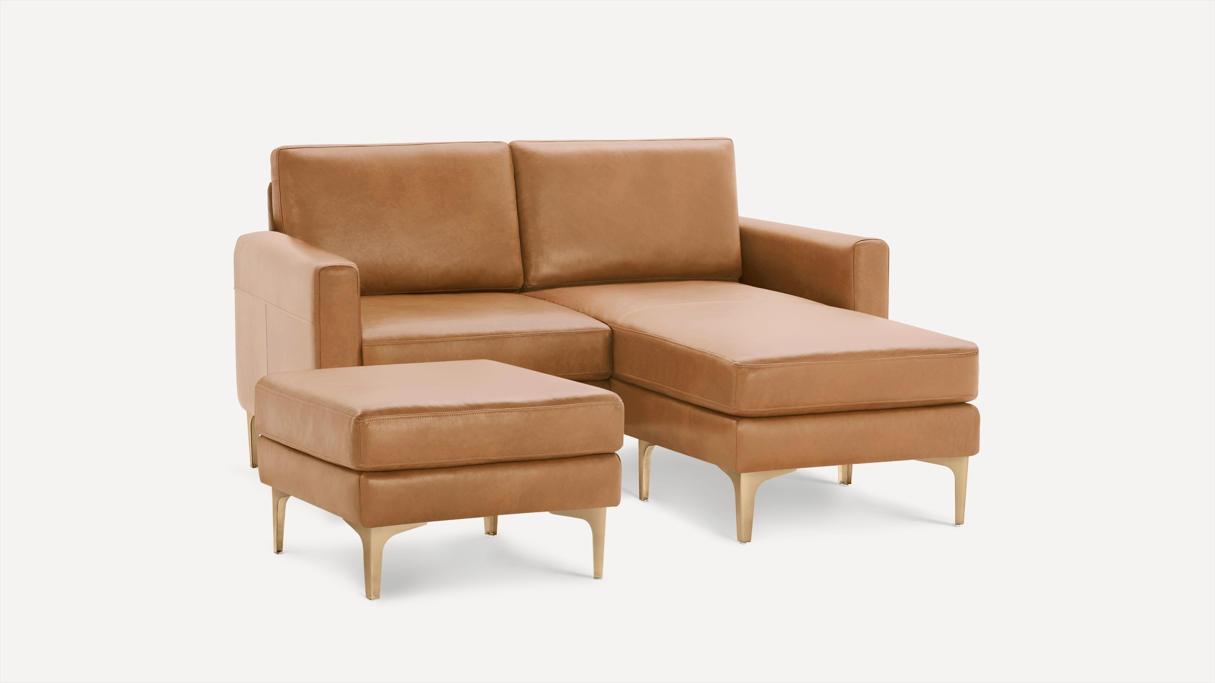 Modern tan leather sectional sofa with gold metal legs, featuring a chaise lounge and a matching ottoman.