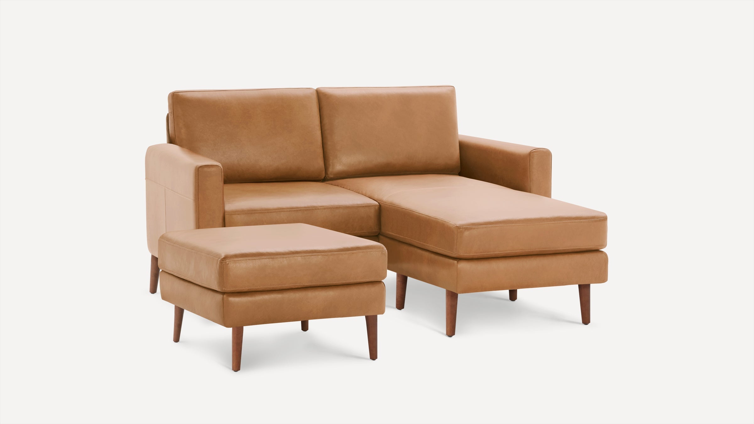 Modern tan leather sectional sofa with chaise lounge and matching ottoman, featuring wooden legs and clean lines.