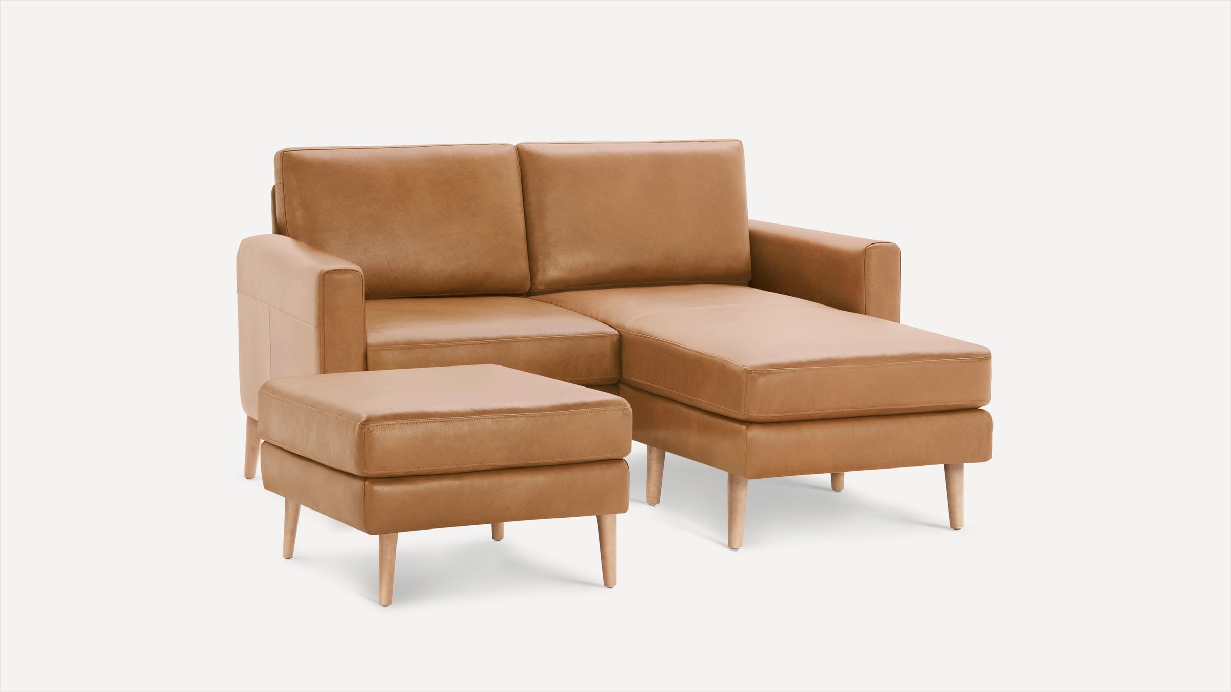 Modern tan leather sectional sofa with matching ottoman, wooden legs, clean lines, and a minimalist design on a white background.