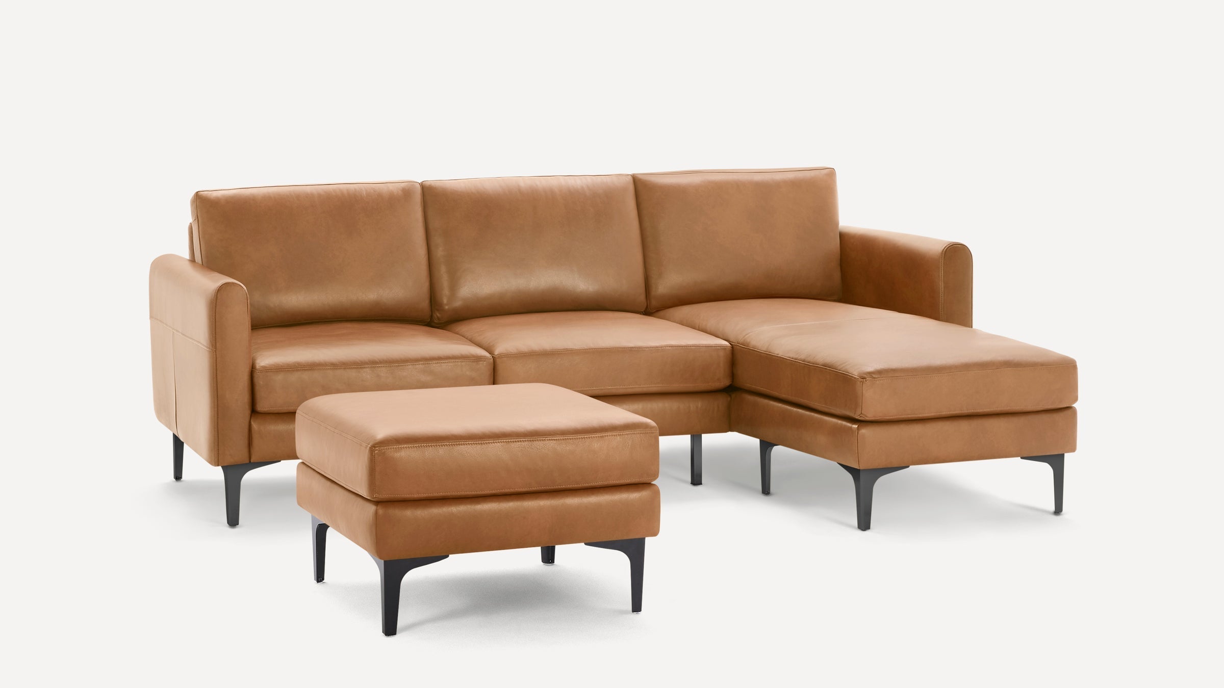 Modern tan leather sectional sofa with chaise lounge and matching ottoman, featuring sleek black metal legs.