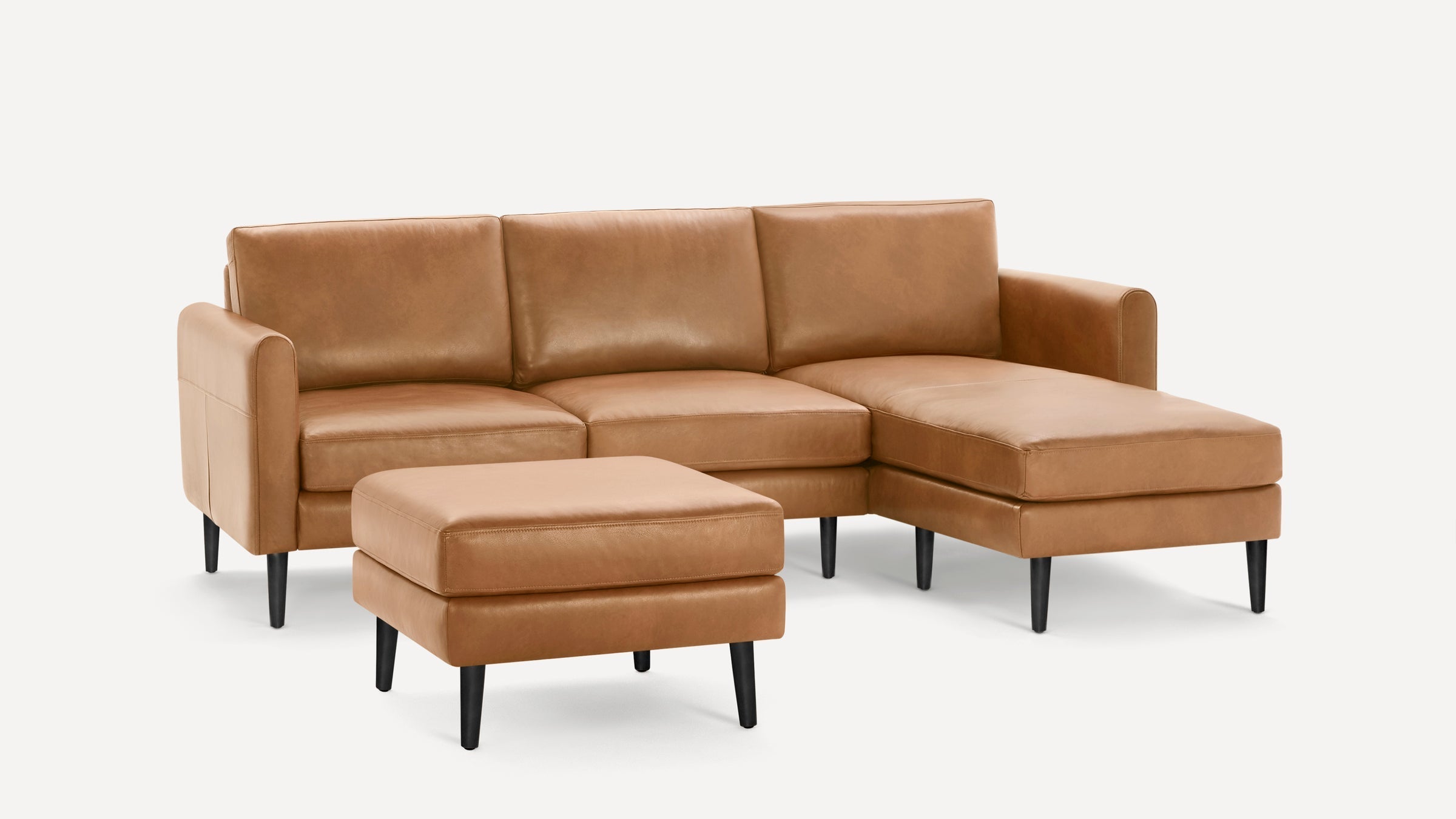Modern tan leather sectional sofa with chaise lounge and matching ottoman, featuring black tapered legs and clean lines.