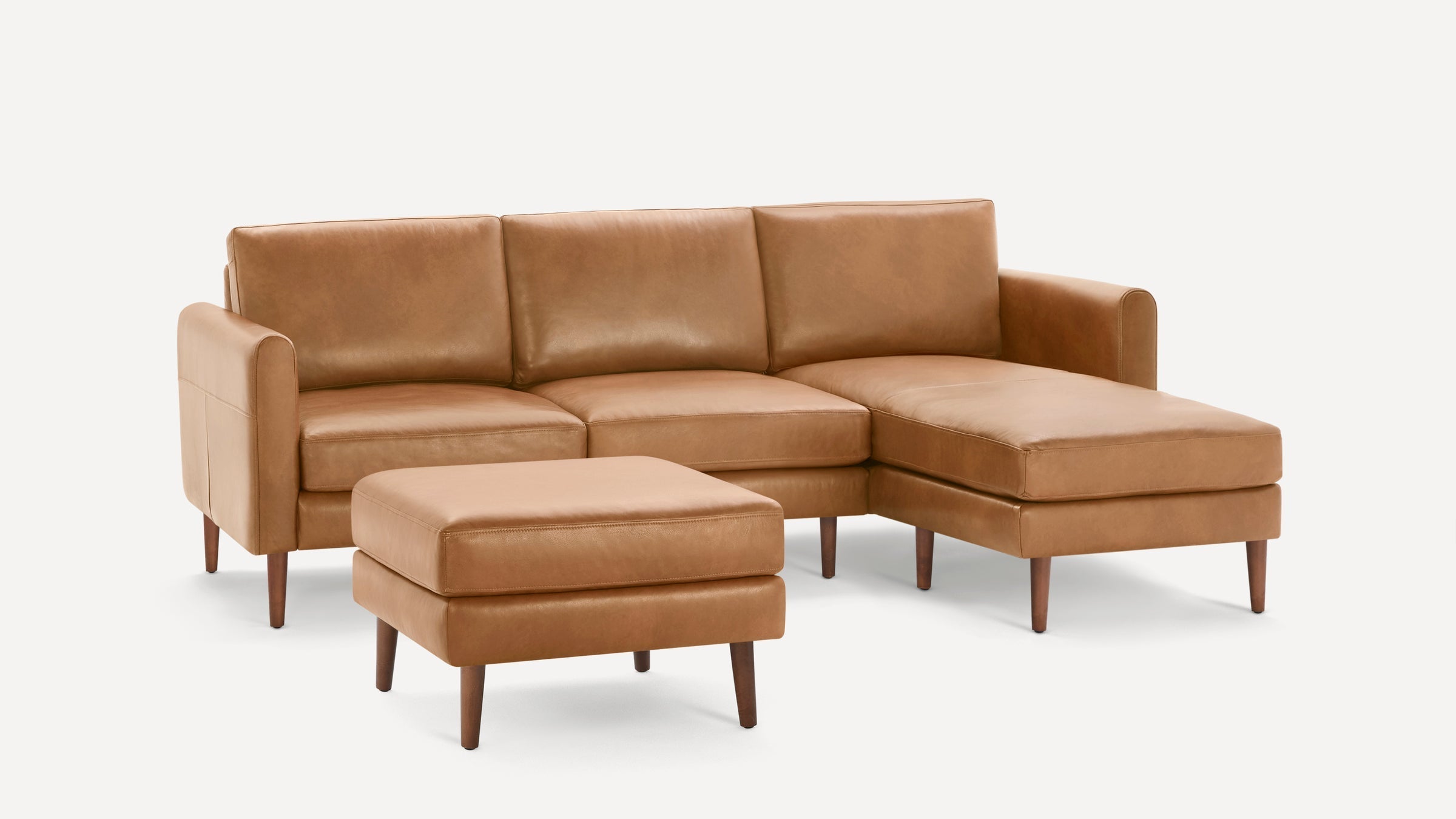 Mid-century modern tan leather sectional sofa with chaise and matching ottoman, featuring wooden tapered legs.