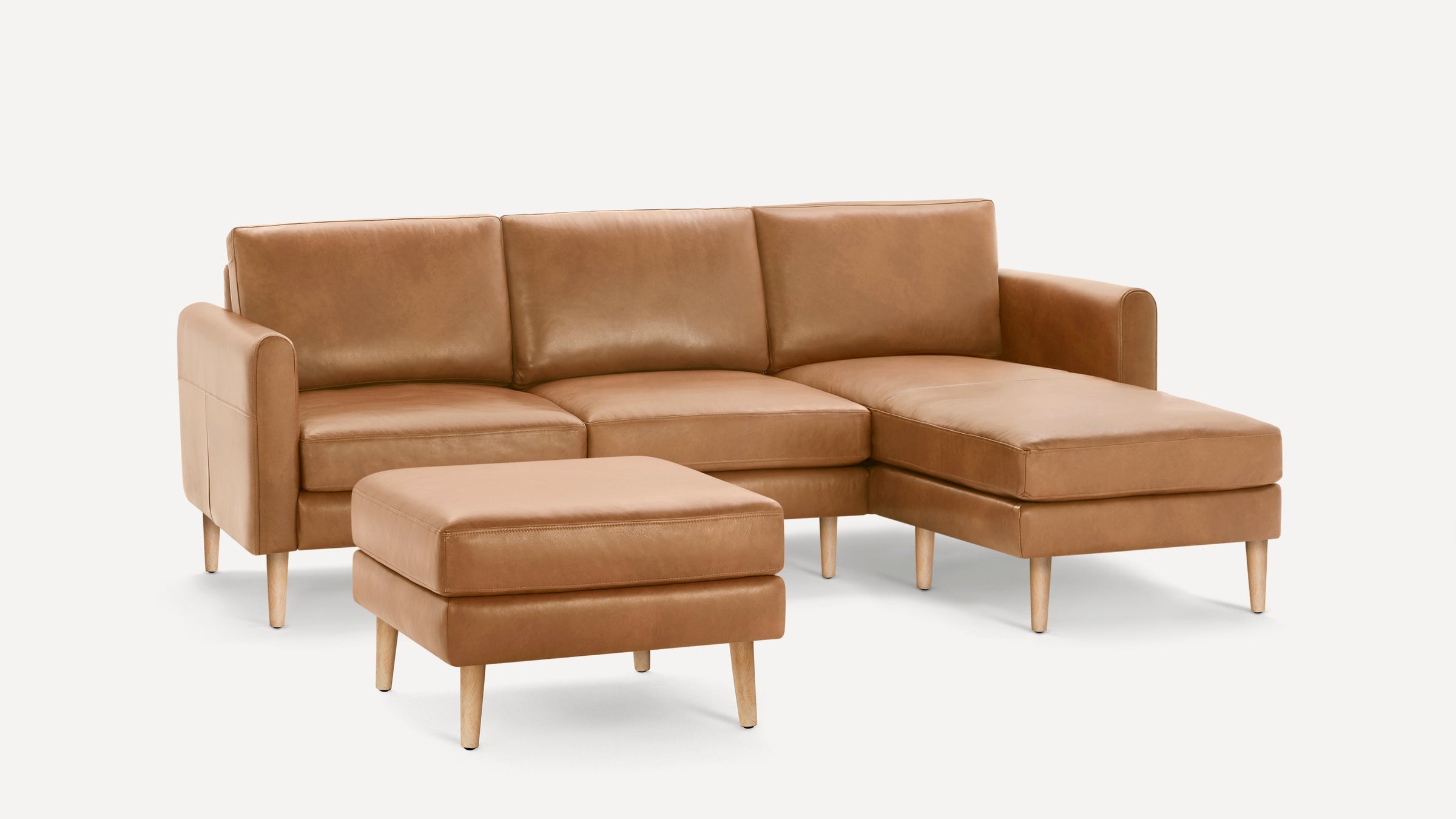 Modern tan leather sectional sofa with chaise and matching ottoman, featuring wooden legs and clean lines.