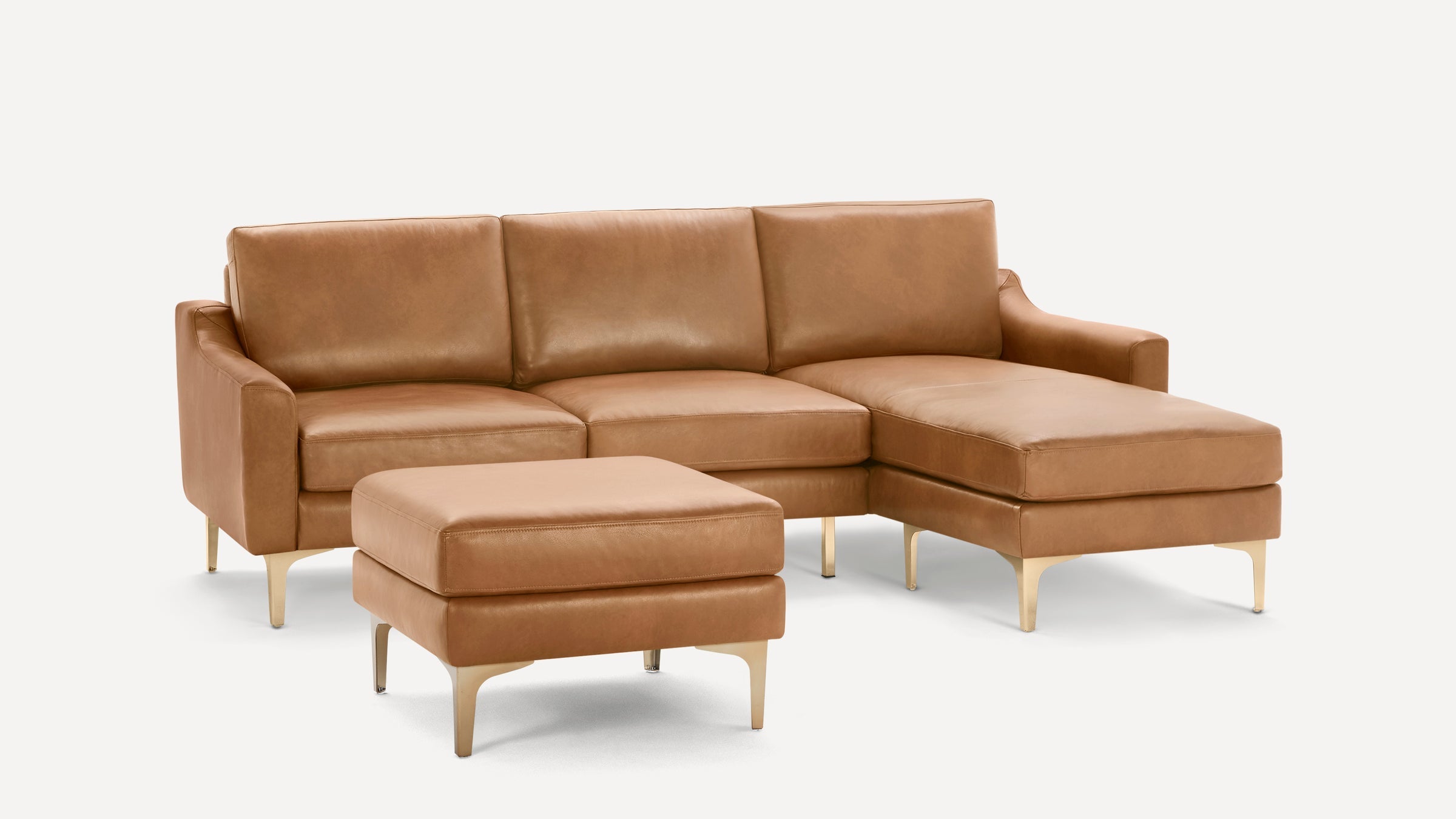 Modern tan leather sectional sofa with chaise lounge and matching ottoman, featuring sleek metal legs.