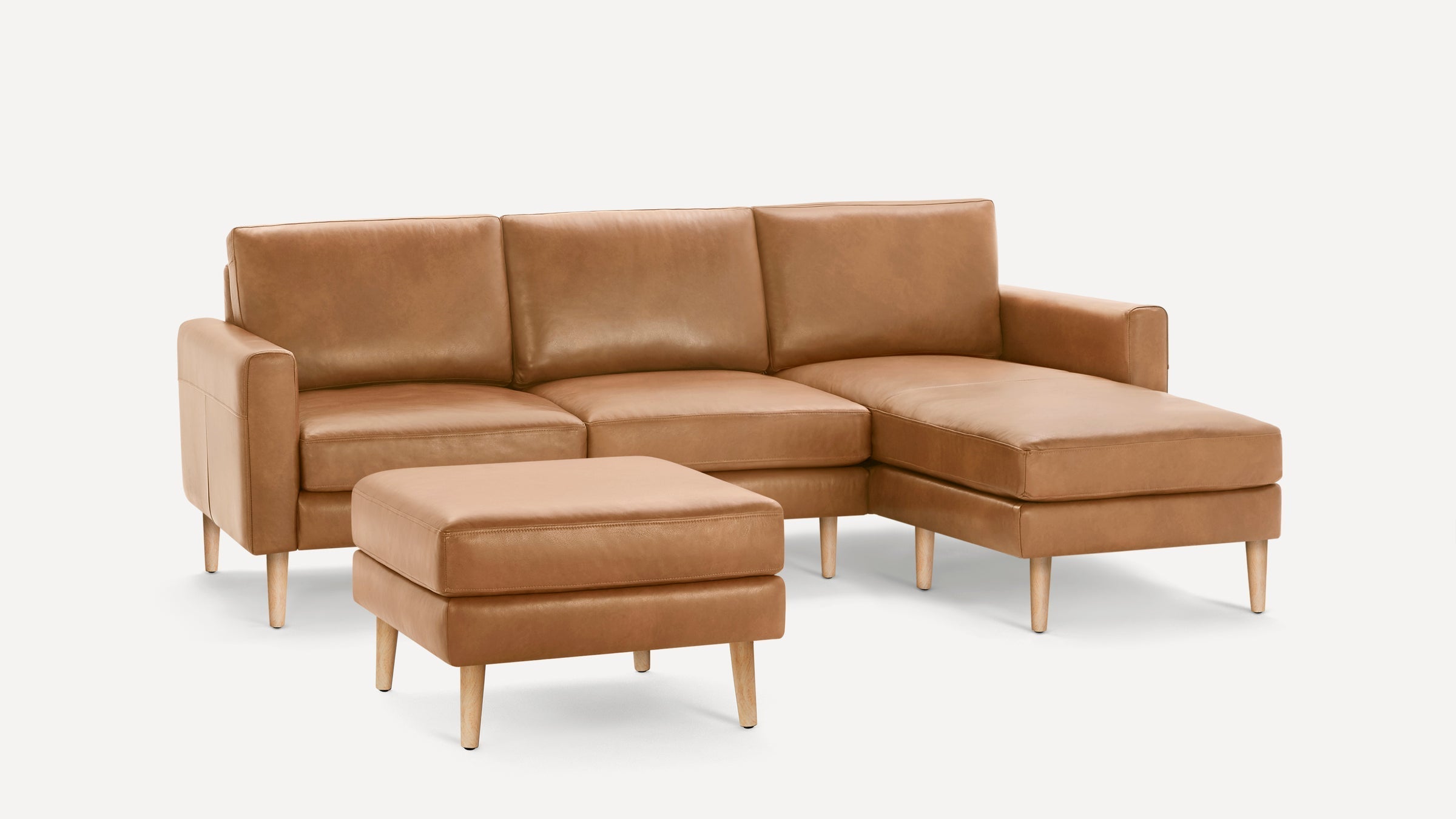 Modern tan leather sectional sofa with chaise and matching ottoman, featuring wooden legs and clean lines.