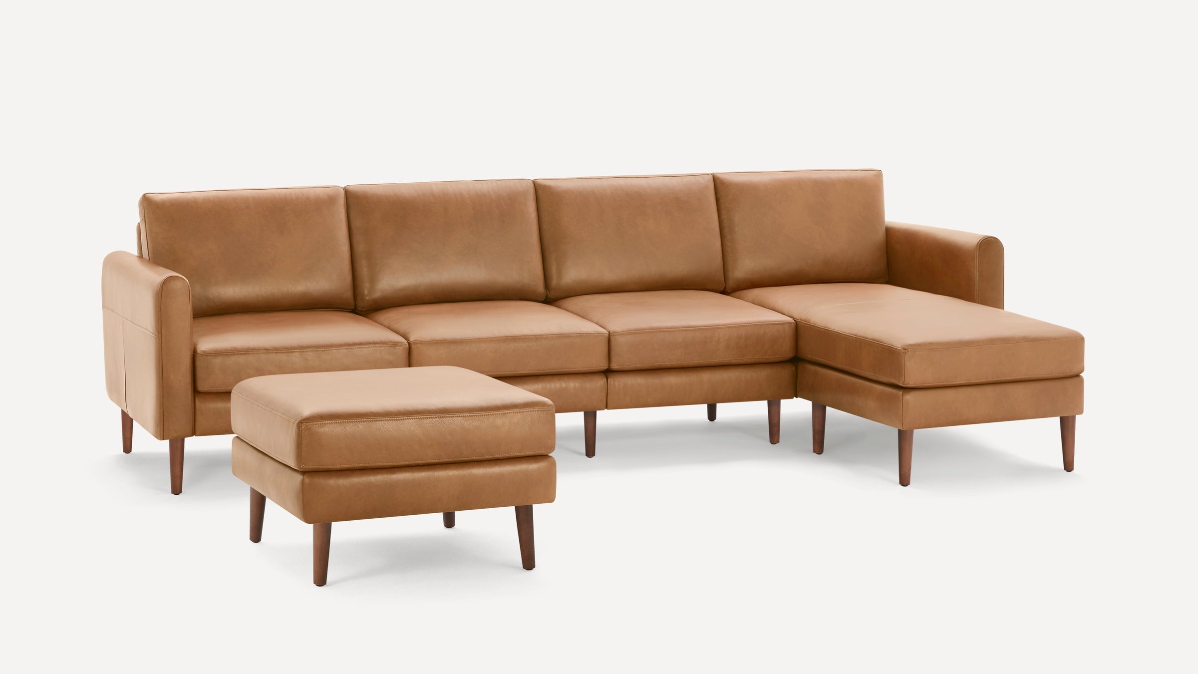 Mid-century modern tan leather sectional sofa with chaise lounge and matching ottoman, featuring wooden tapered legs.