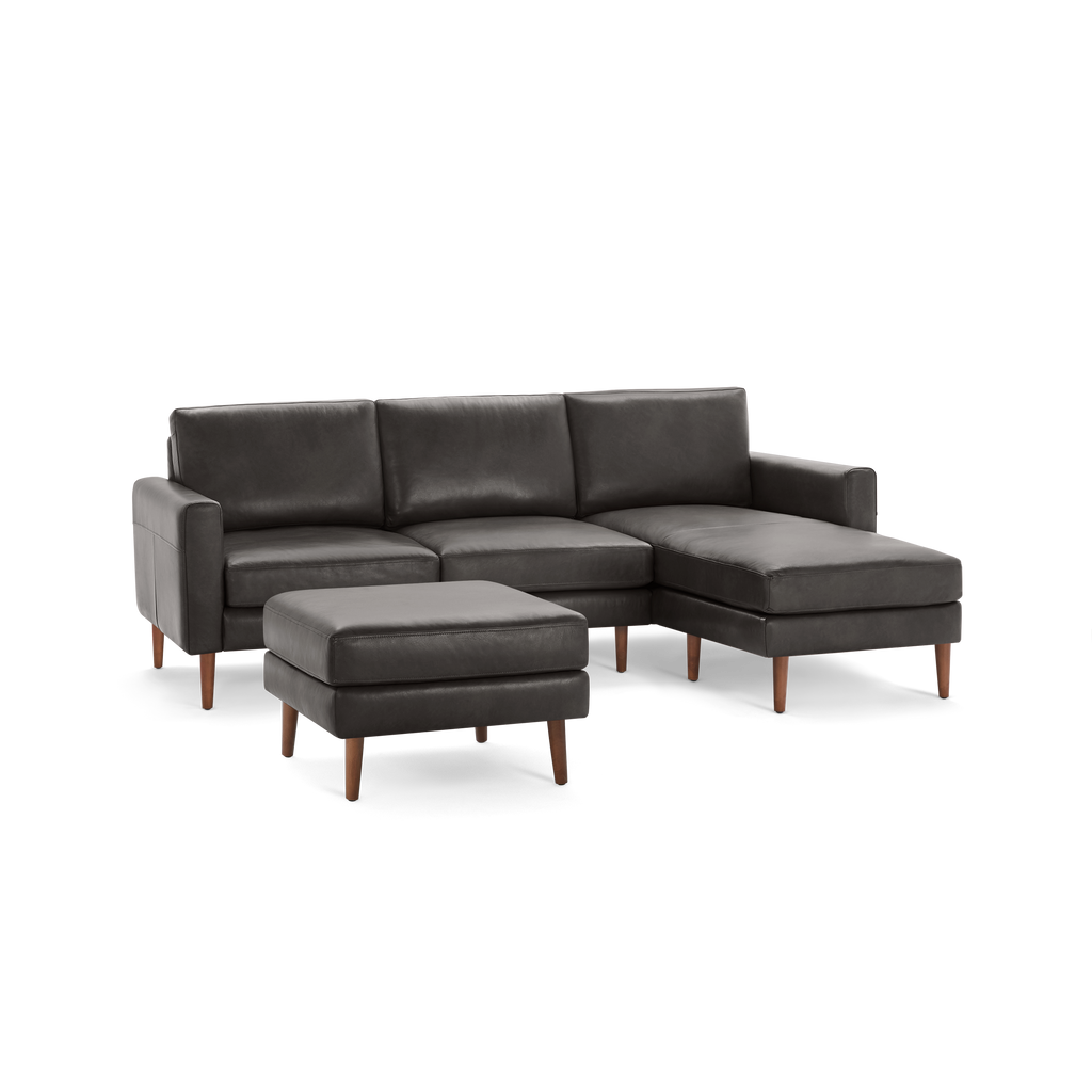 Dark gray leather sectional sofa with matching ottoman, wooden legs, and modern design spacious chaise lounge on right side.