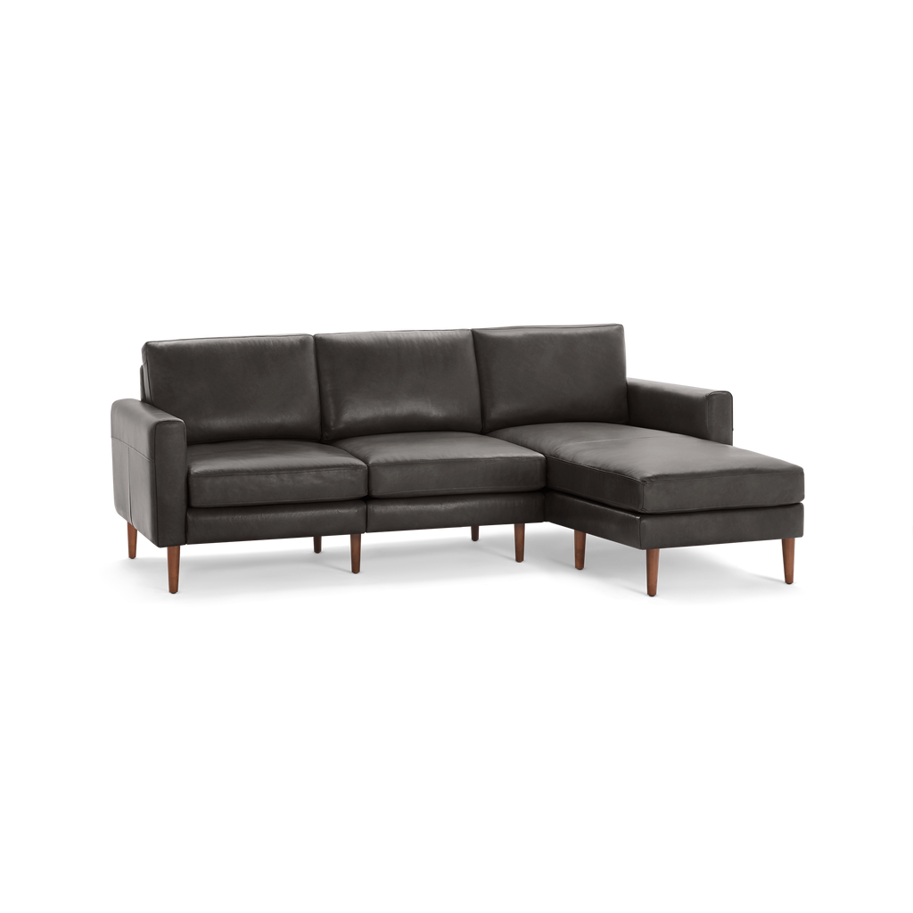 Dark gray leather sectional sofa with three cushions and wooden legs, featuring a chaise lounge on the right side.