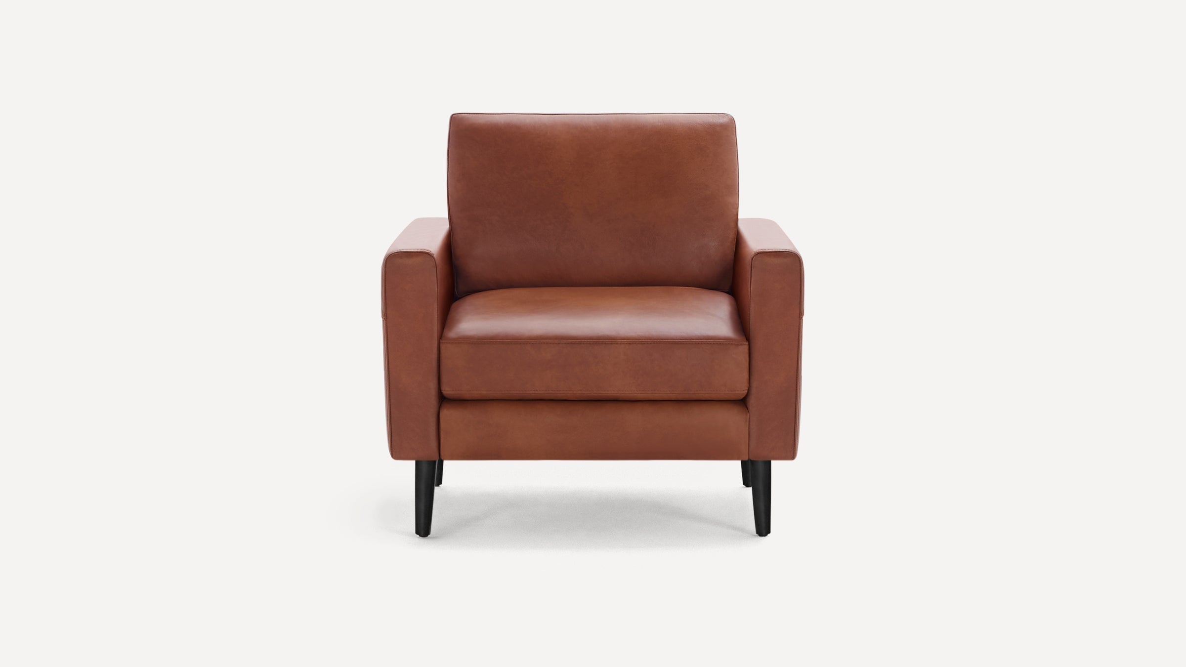 Front view of a modern brown leather armchair with black tapered wooden legs and square armrests.