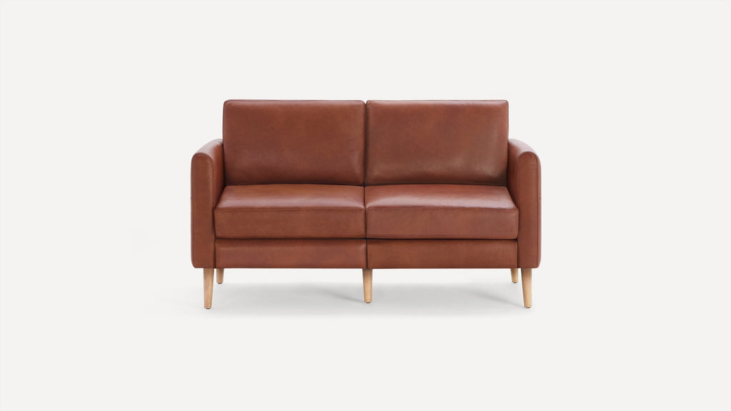 Mid-century modern two-seater sofa with smooth brown leather upholstery and light wooden tapered legs on a white background.