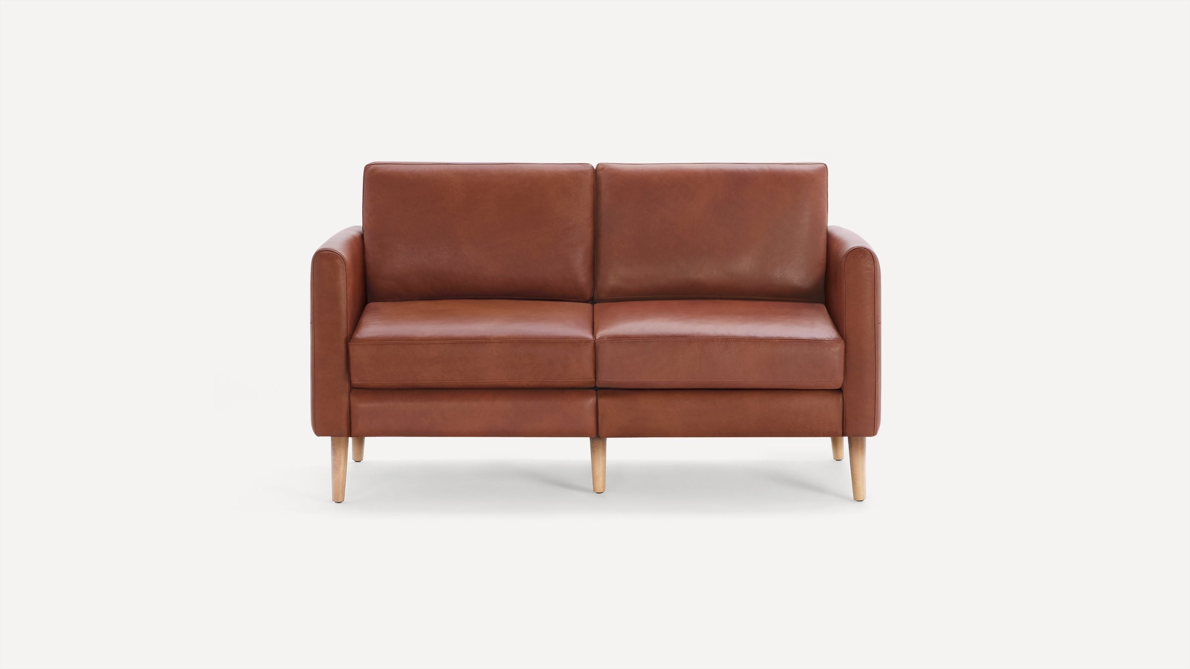Mid-century modern two-seater sofa with smooth brown leather upholstery and light wooden tapered legs on a white background.