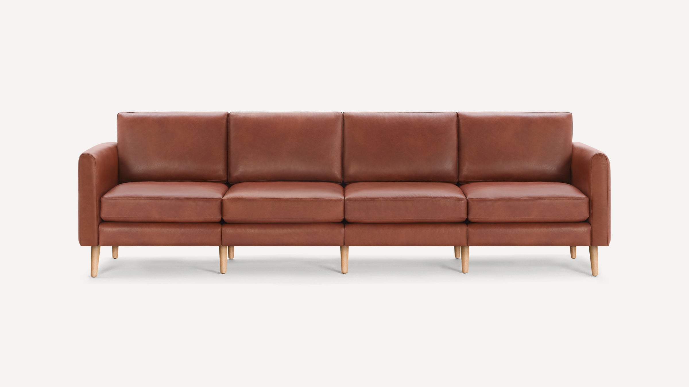 Brown leather four-seater sofa with wooden legs, cushioned seats, and padded armrests, set against a plain white background.