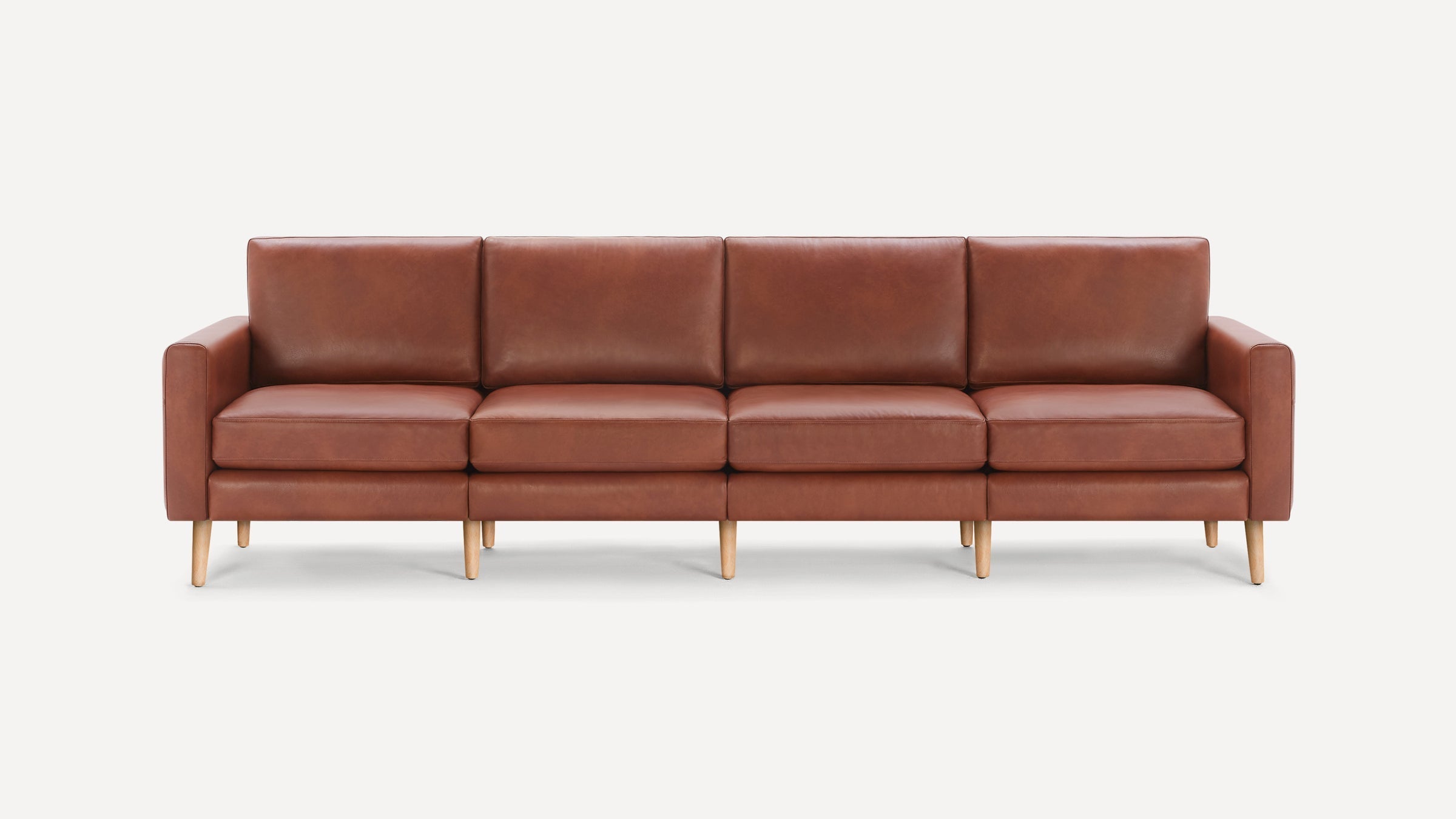 Four-seater brown leather sofa with straight armrests, cushioned seats, and light wooden tapered legs on white background.