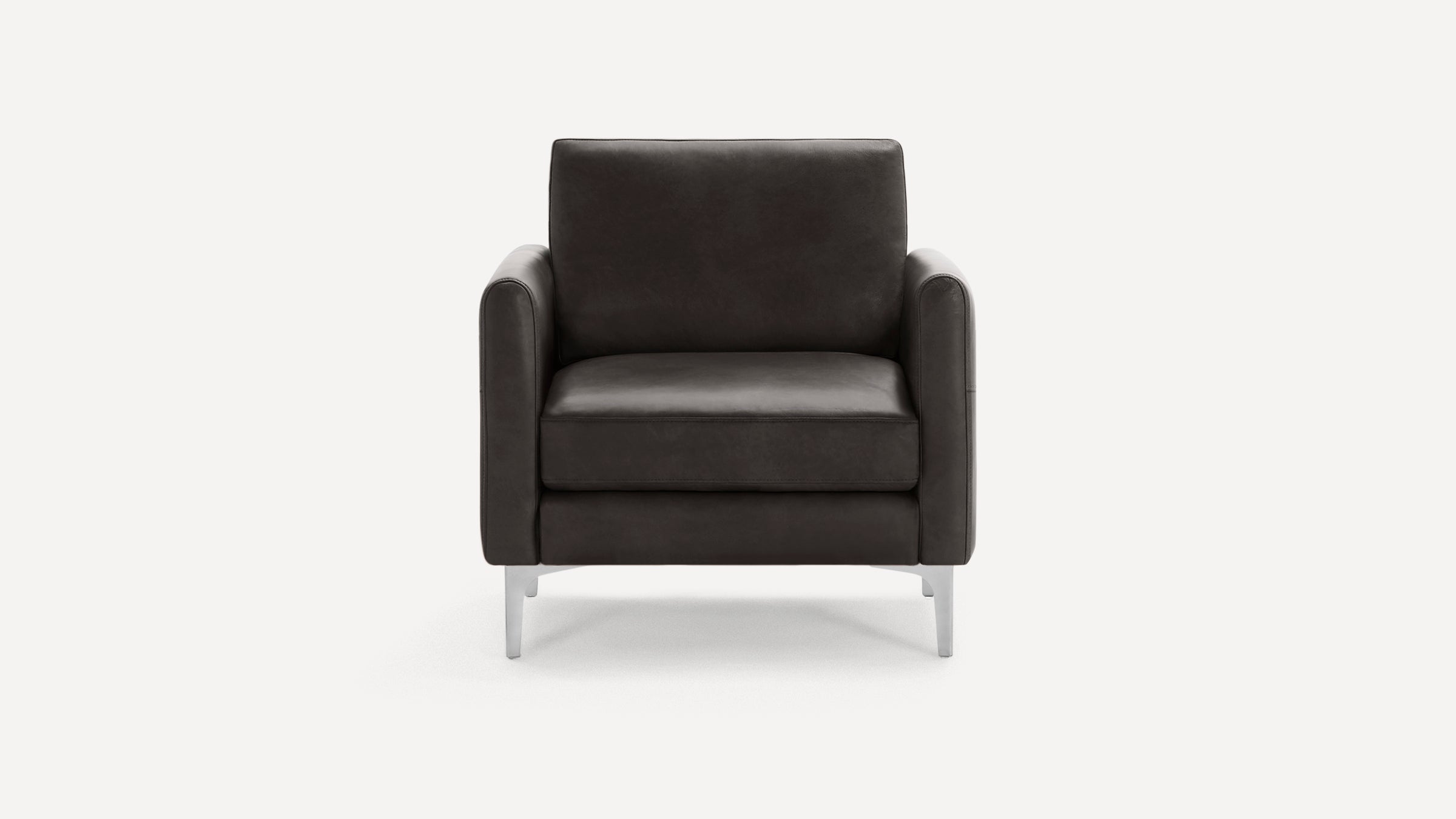 Front view of a modern dark gray leather armchair with boxy cushions and slim metal legs on a white background.