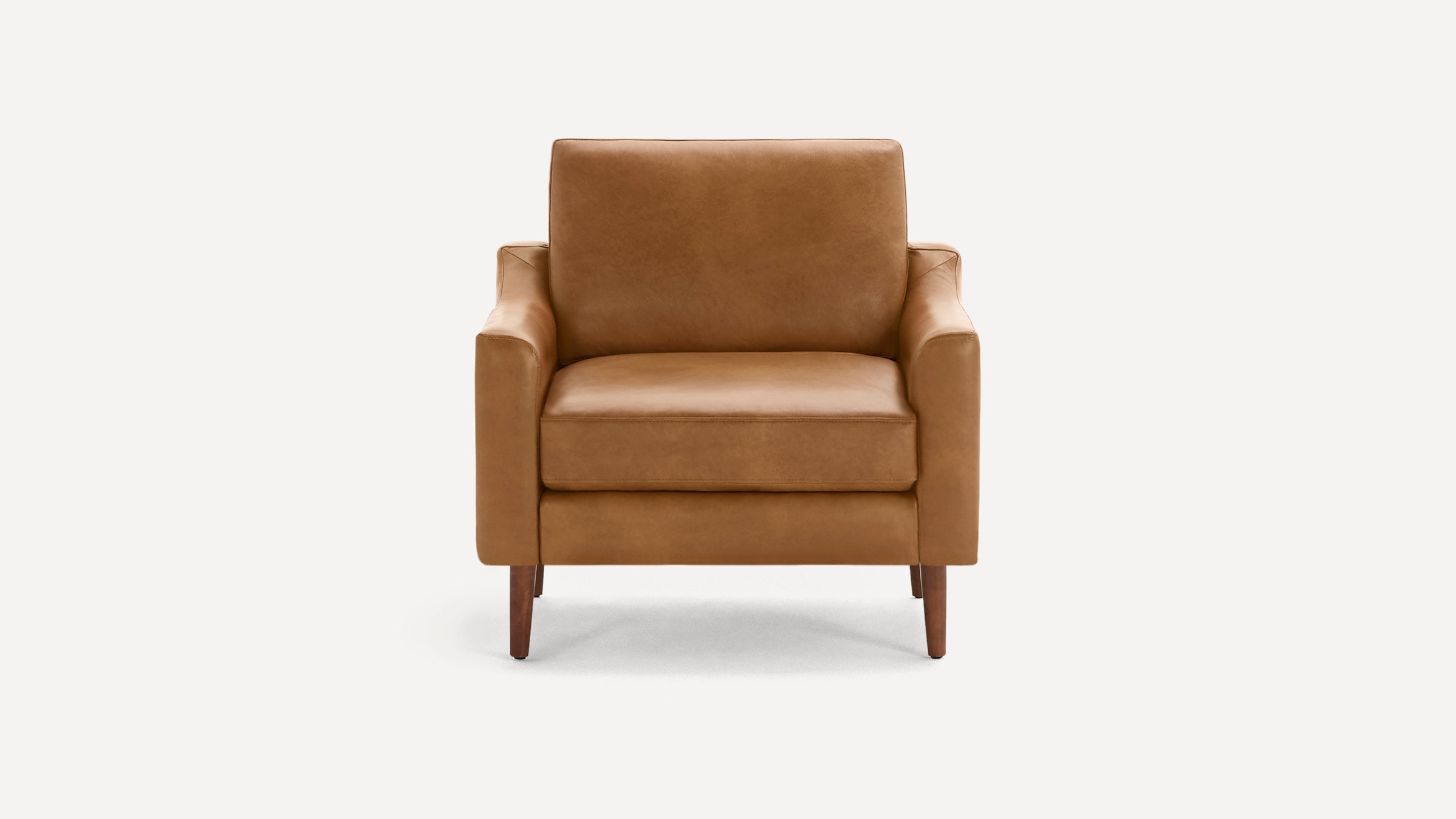 Front view of a modern, tan leather armchair with straight arms and wooden legs on a white background.