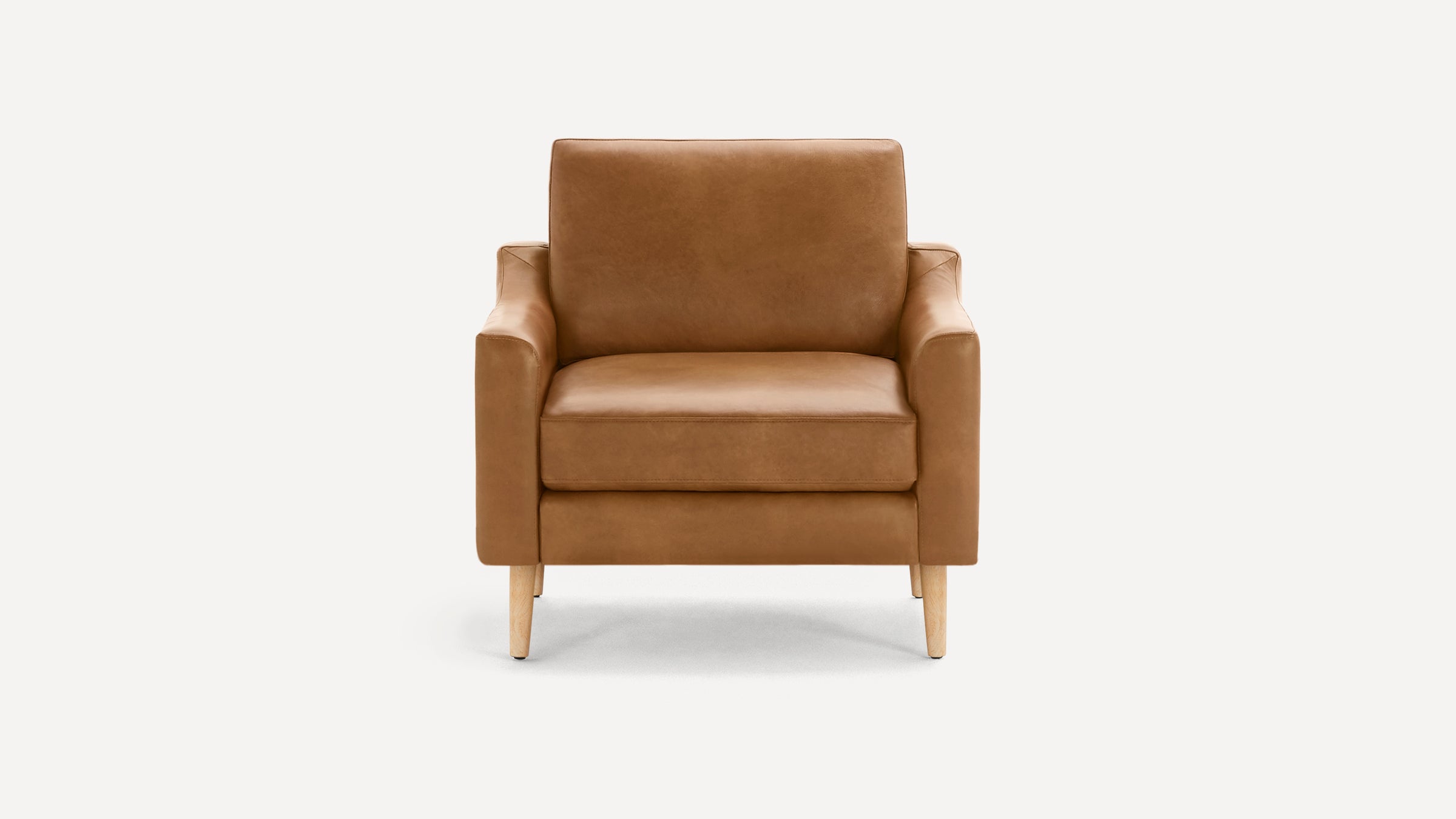 Mid-century modern armchair in tan leather with cushioned seat, backrest, and light wooden legs on white background.