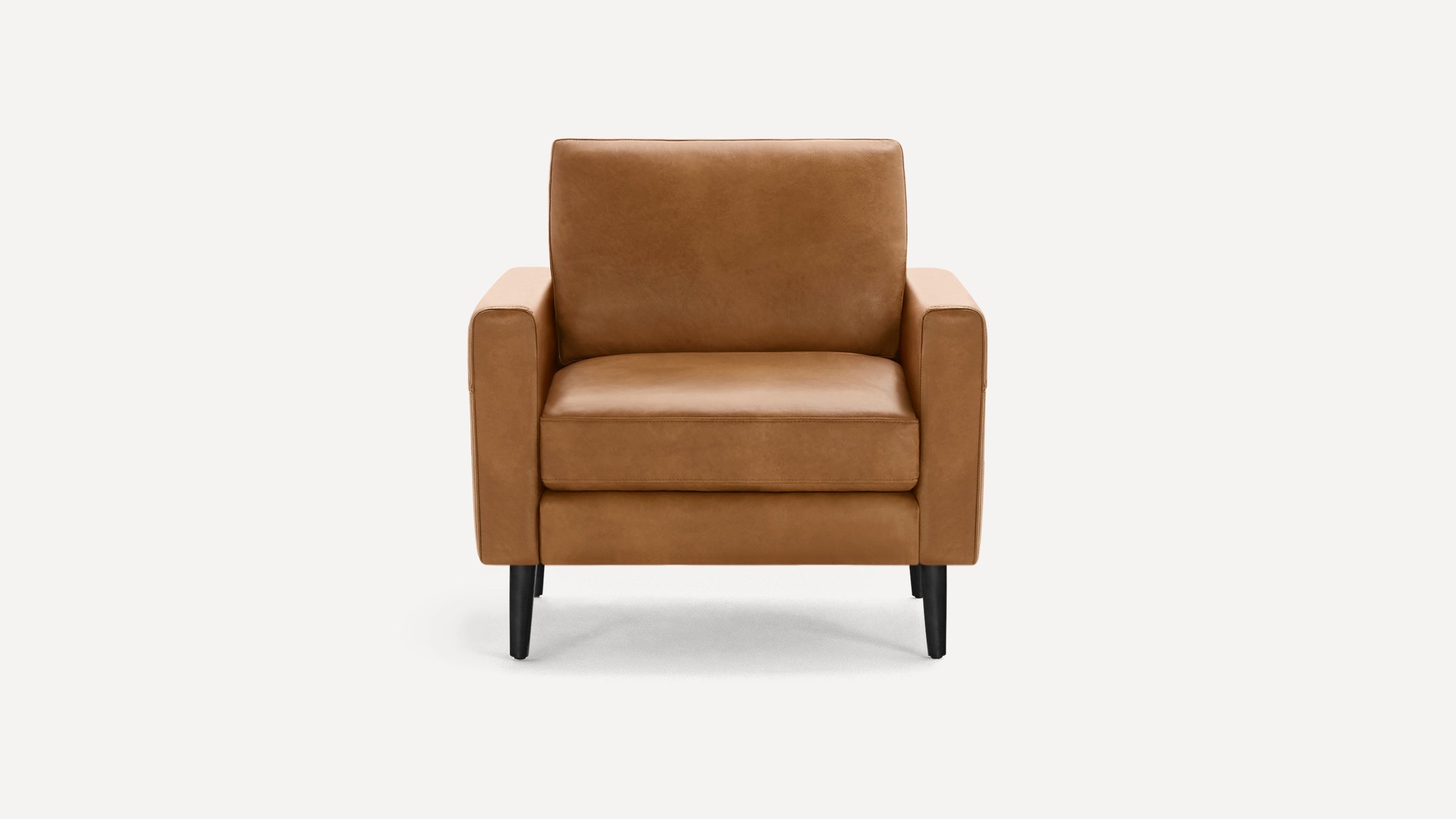 Front view of a modern tan leather armchair with square arms and black tapered wooden legs on a white background.