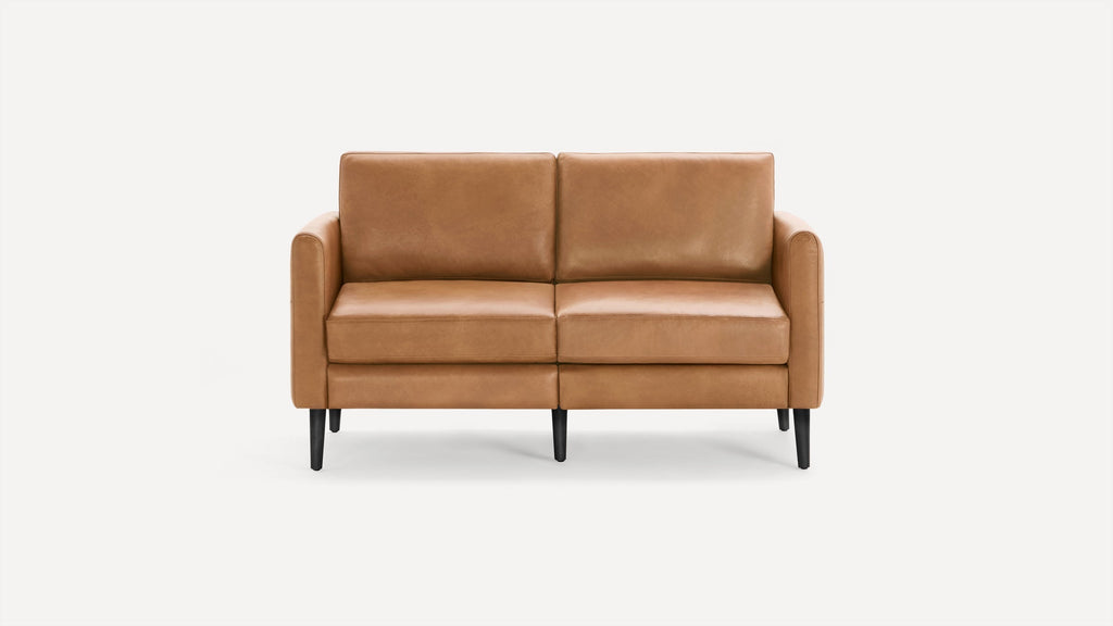 Modern two-seater sofa with smooth caramel-brown leather upholstery and black tapered wooden legs against a white background.