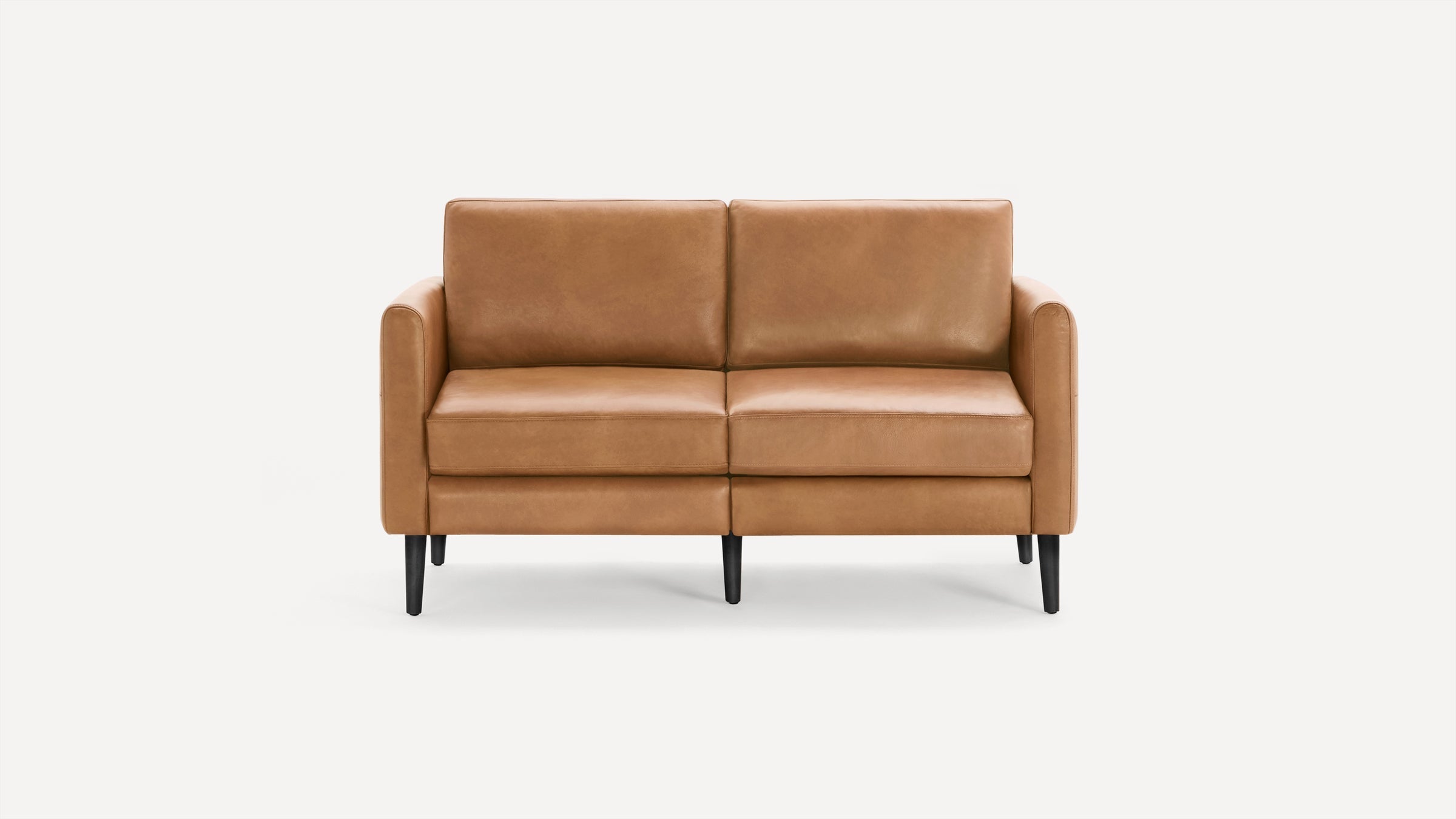 Modern two-seater sofa with smooth caramel-brown leather upholstery and black tapered wooden legs against a white background.