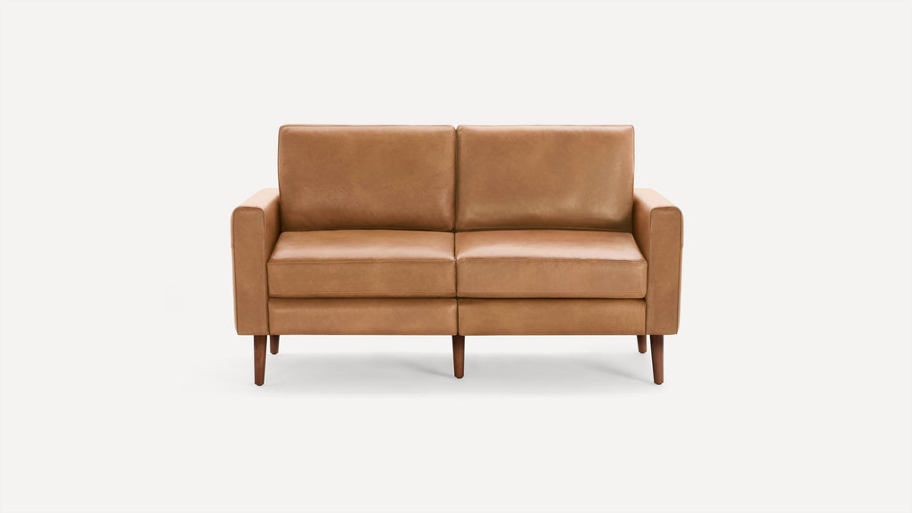 Mid-century modern tan leather two-seater sofa with straight arms and wooden tapered legs, isolated on white background.