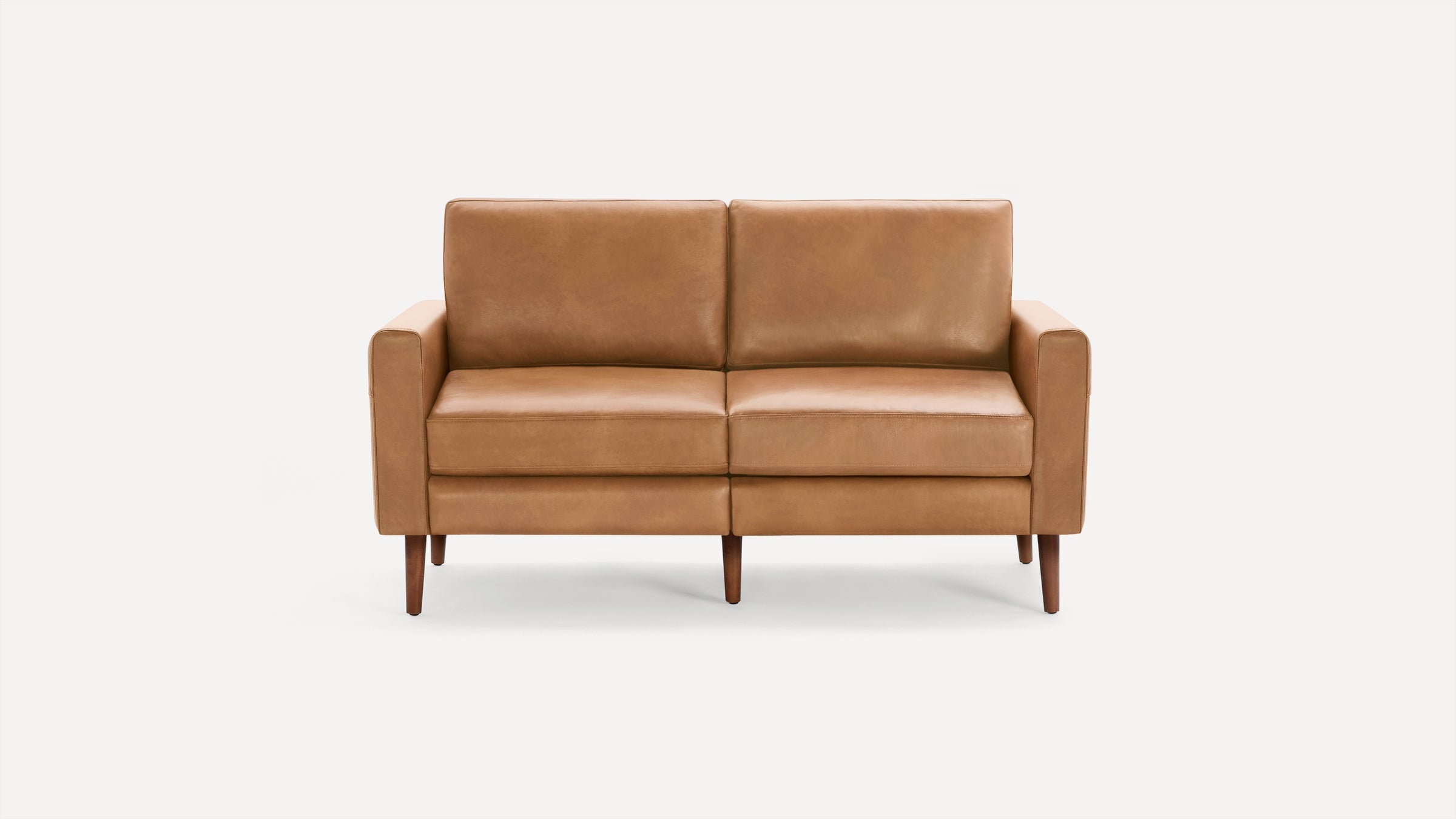 Mid-century modern tan leather two-seater sofa with straight arms and wooden tapered legs, isolated on white background.