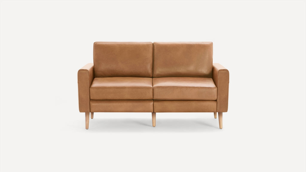 Mid-century modern style two-seater sofa in light brown leather with straight arms and wooden legs against a plain white background.