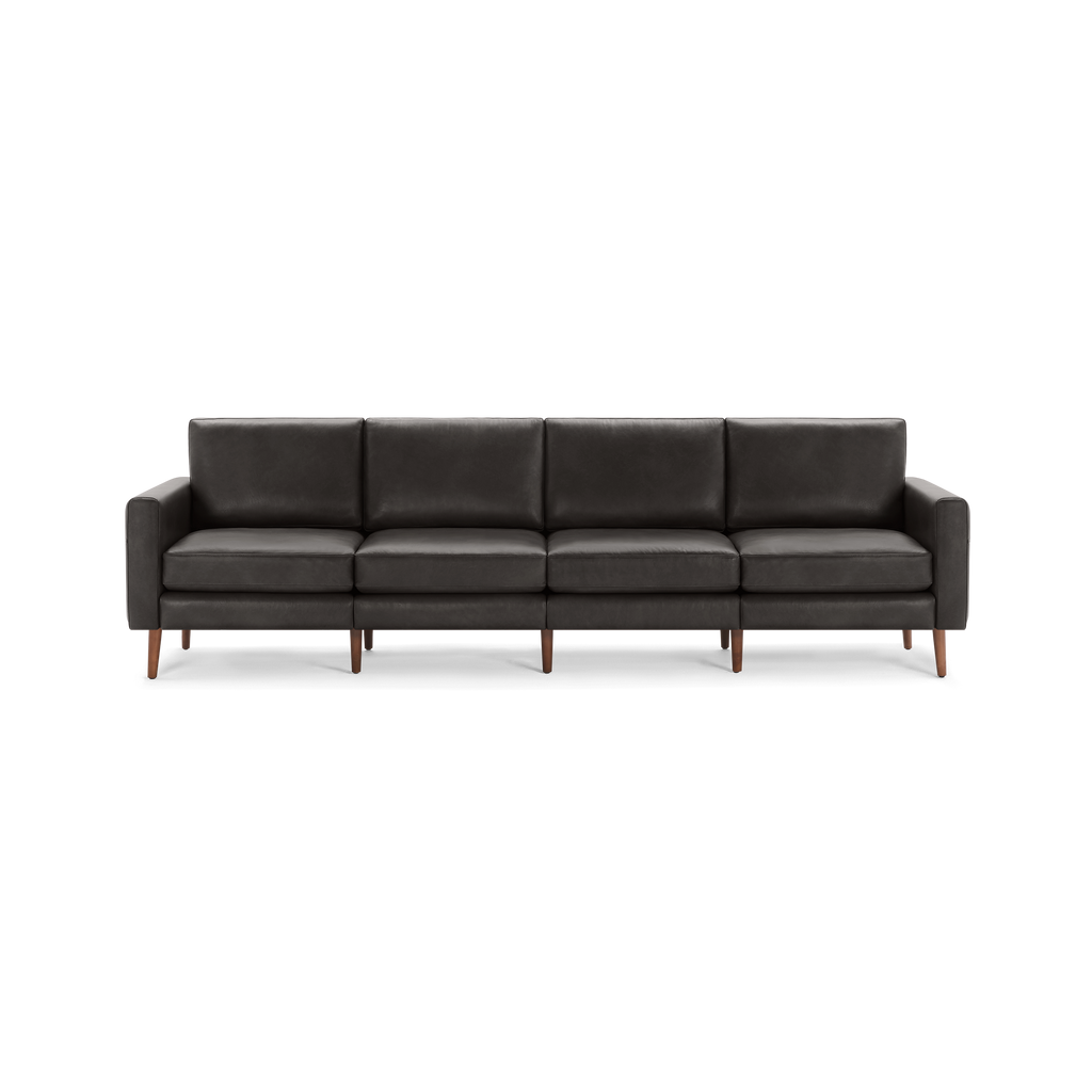 Modern long dark gray leather sofa with four seat cushions, straight armrests, and wooden legs, isolated on a white background.