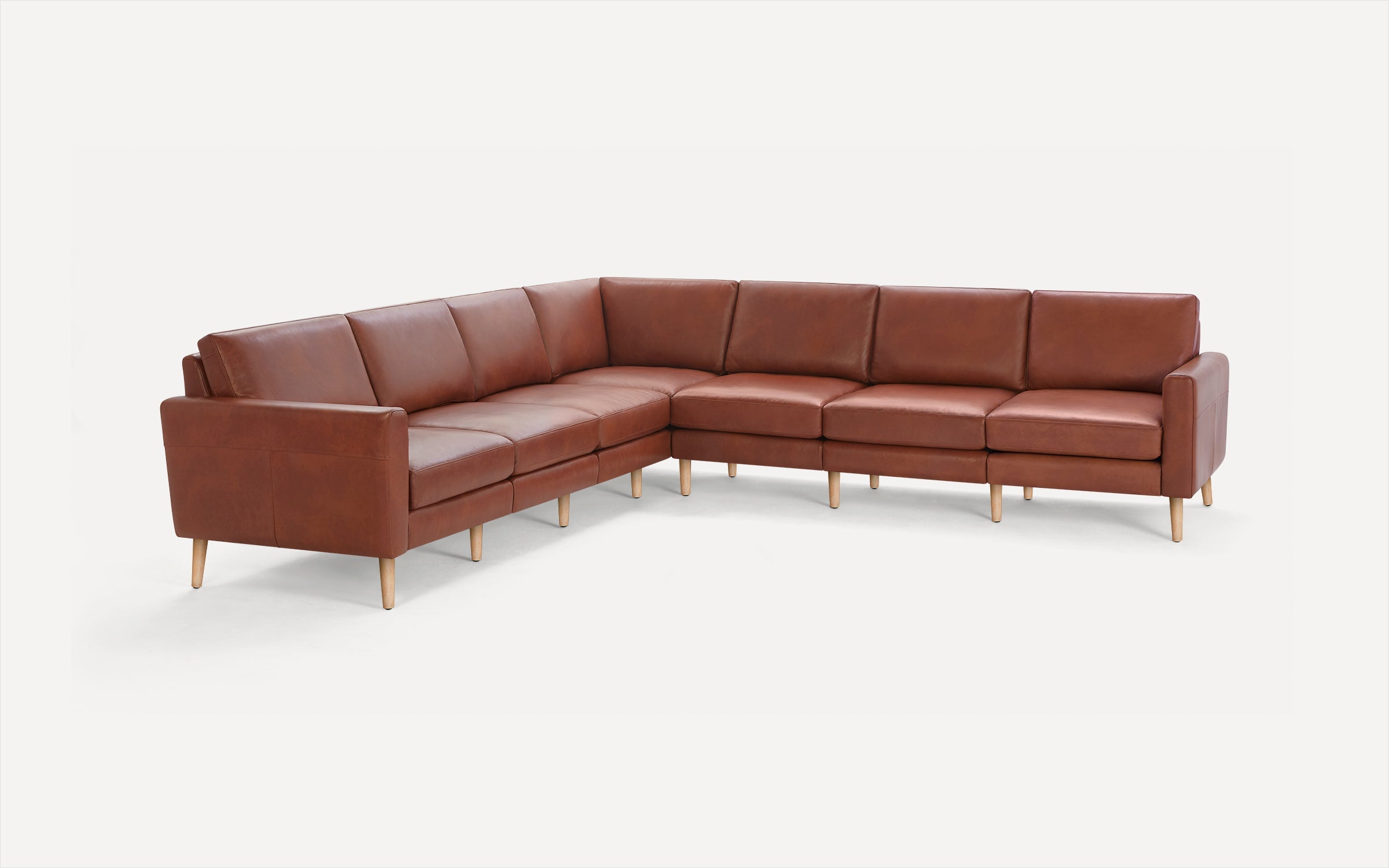 Large L-shaped sectional sofa in warm brown leather with wooden legs and clean, modern design.