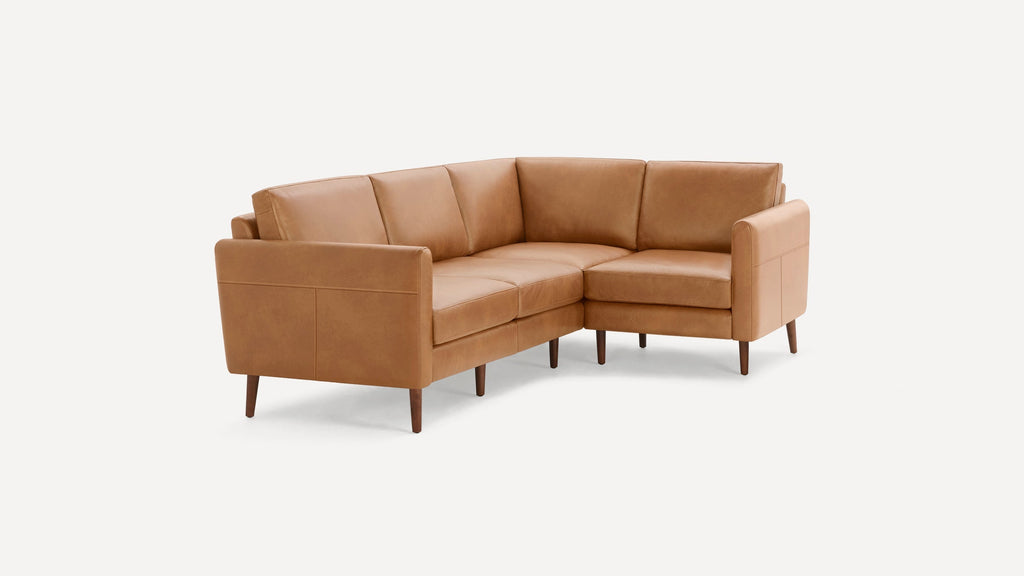 Tan leather L-shaped sectional sofa with cushioned seats and backs, supported by dark wooden tapered legs.