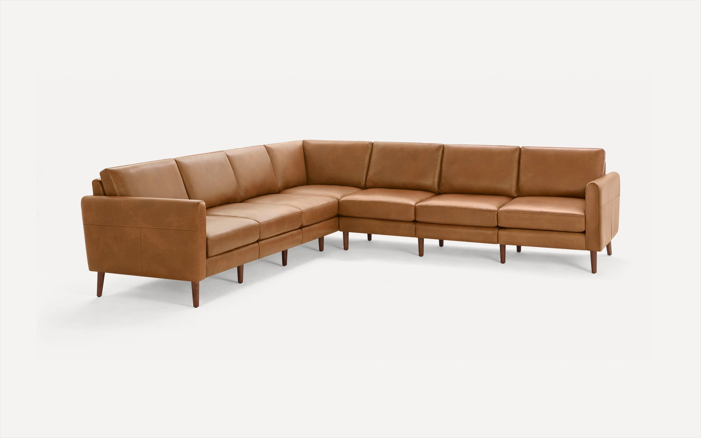 Large L-shaped sectional sofa with tan leather upholstery and wooden tapered legs on a white background.