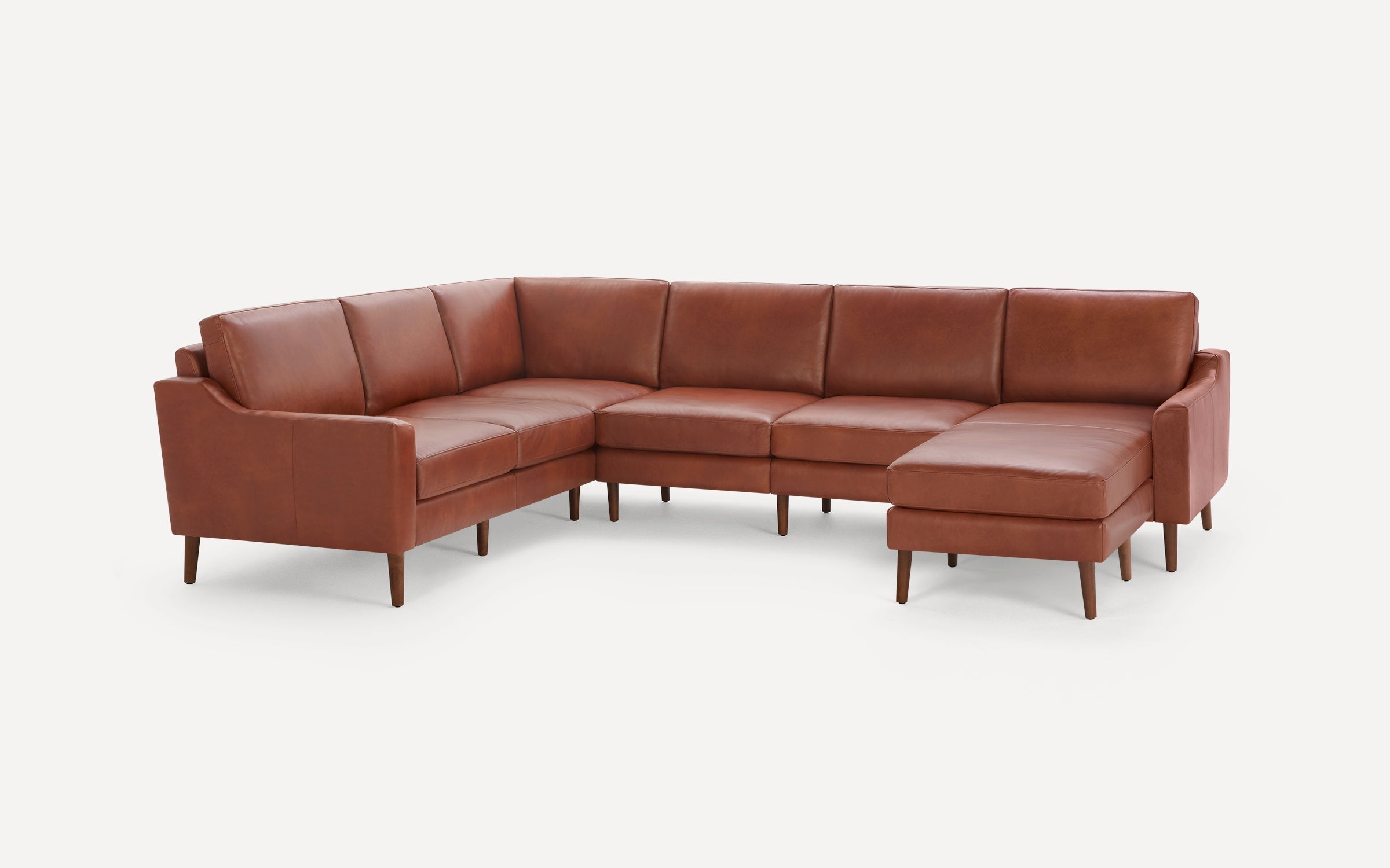 Modern brown leather sectional sofa with a chaise lounge on the right side and tapered wooden legs on a white background.