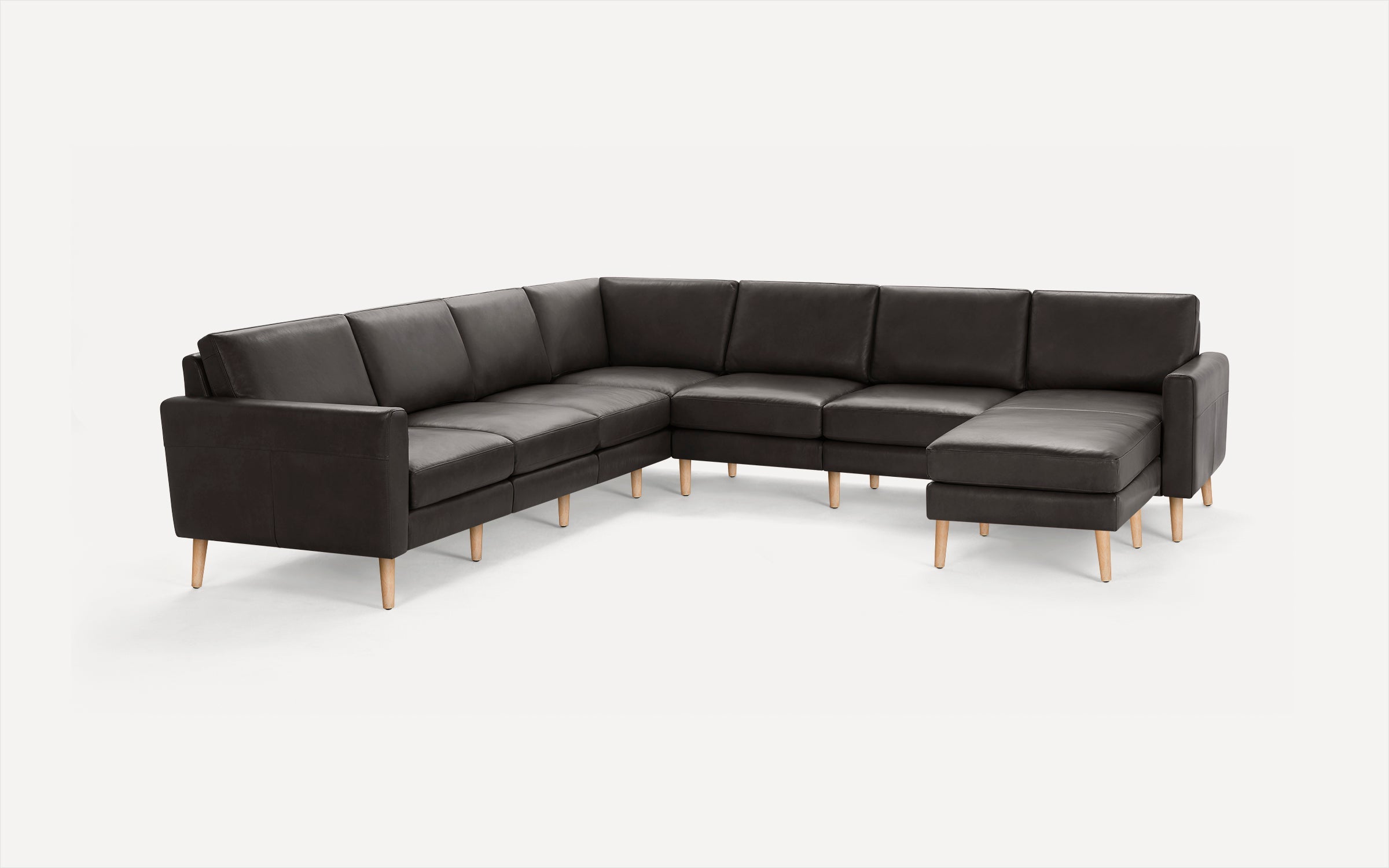 Large modern L-shaped sectional sofa in dark gray leather with wooden legs, featuring a chaise lounge on the right side.