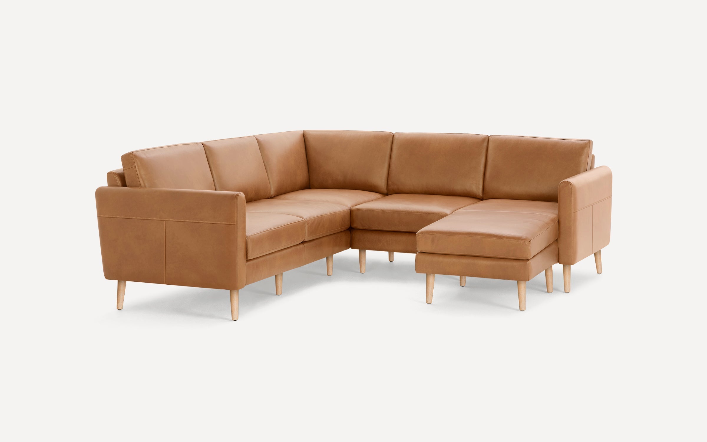 Mid-century modern L-shaped sectional sofa with caramel brown leather upholstery and light wooden legs against a plain white background.