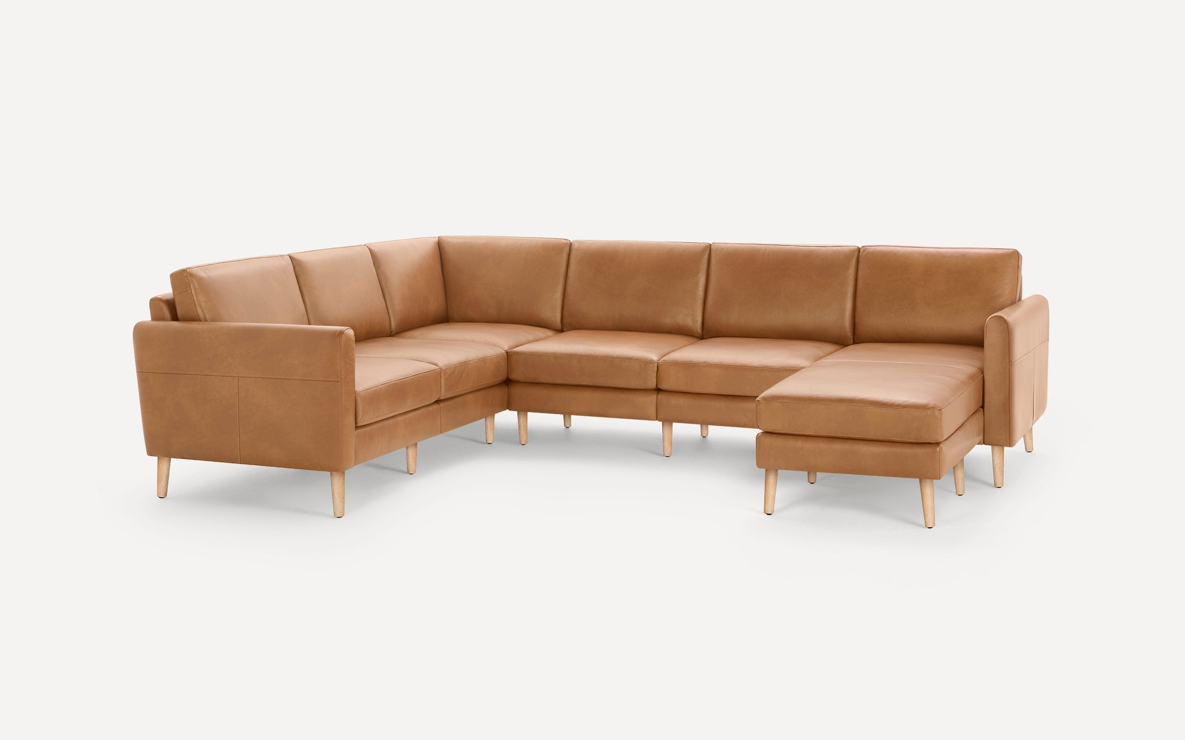 Large L-shaped sectional sofa with tan leather upholstery and light wooden legs, featuring clean, modern design and cushioned seats.