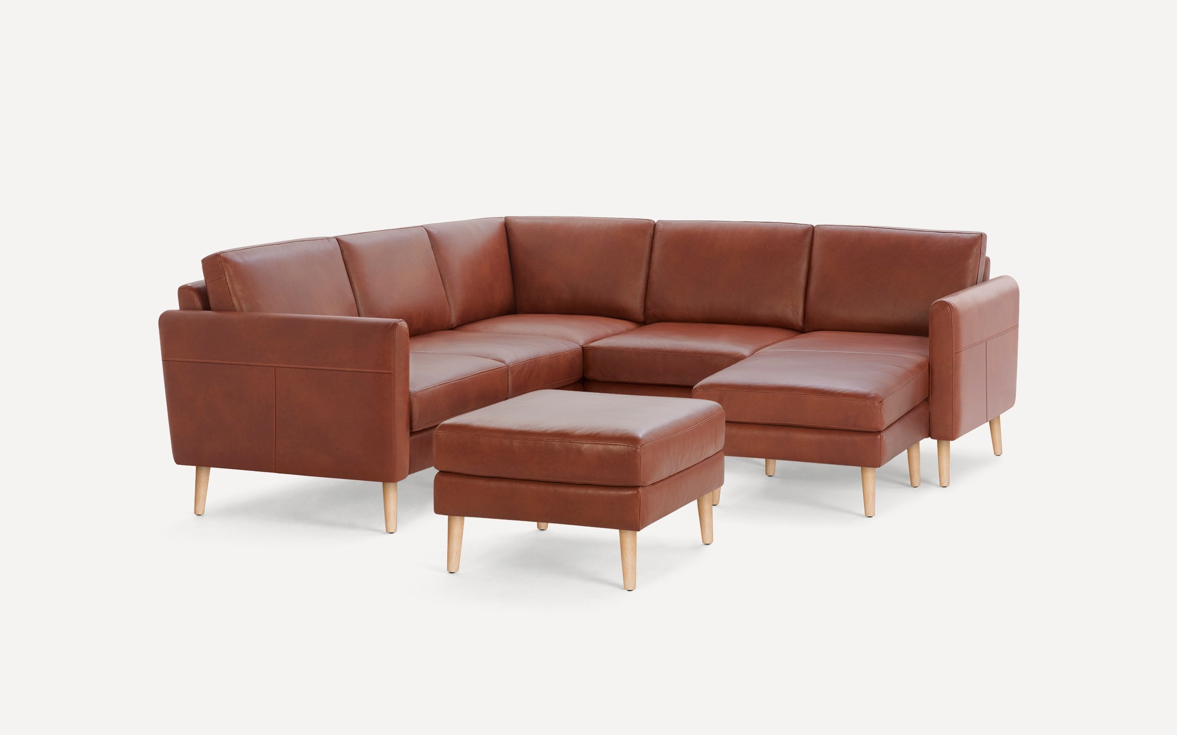 Modern L-shaped brown leather sectional sofa with matching ottoman, wooden legs, and clean lines on white background.