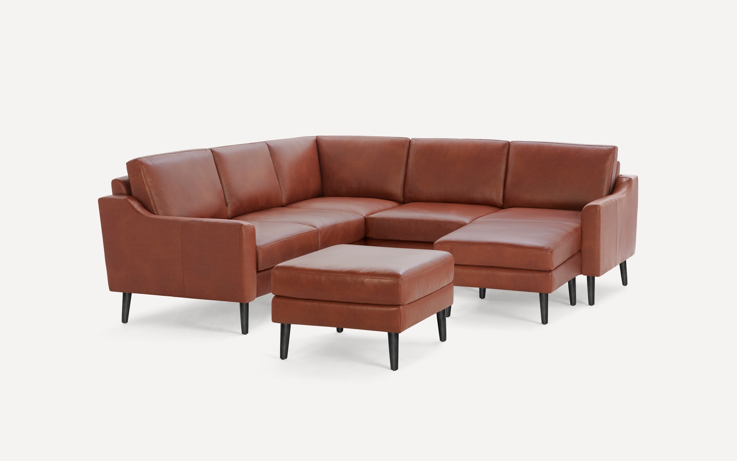 Brown leather sectional sofa with modern black tapered legs and matching ottoman on white background.