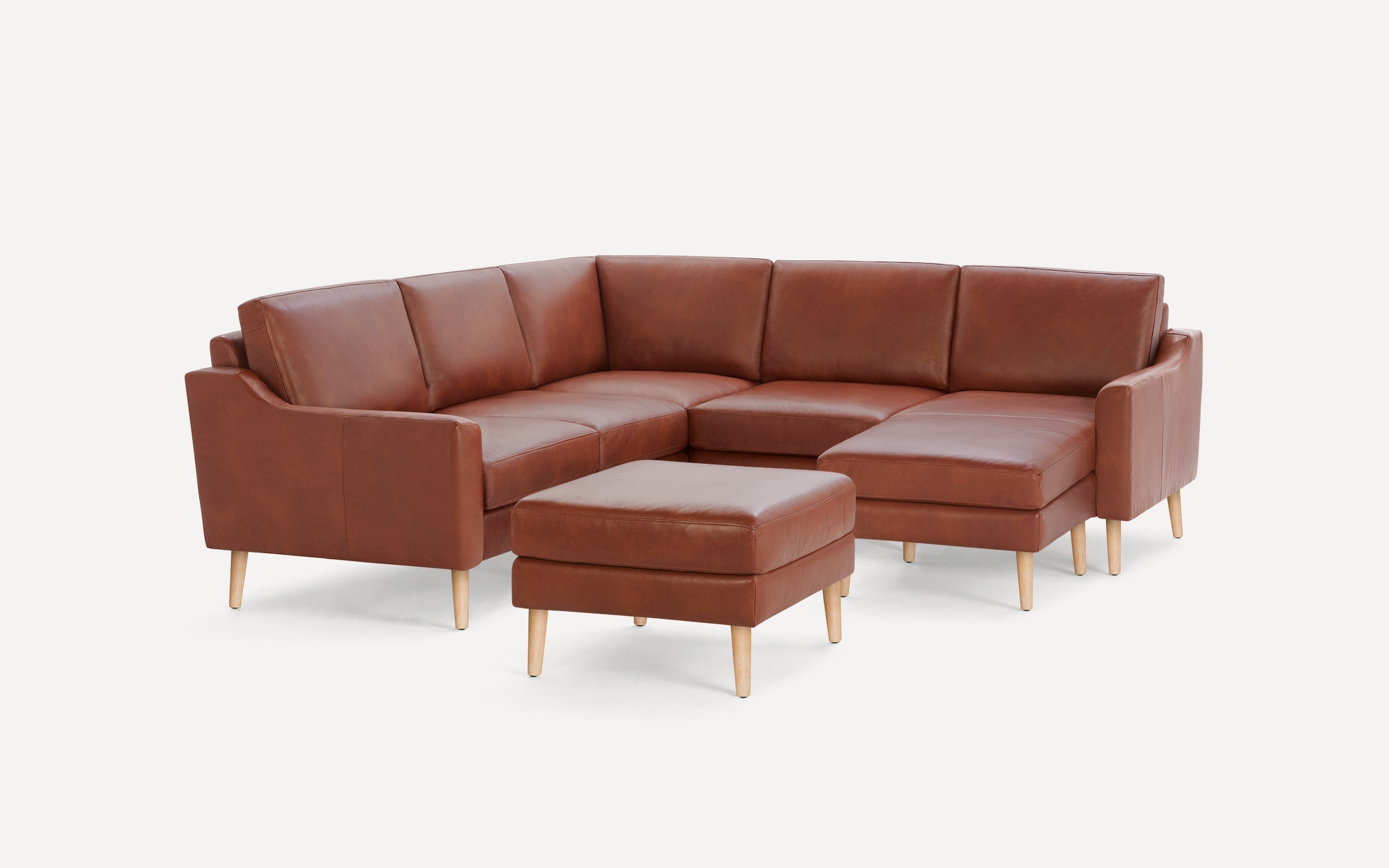 Brown leather sectional sofa with wooden legs and a matching ottoman against a white background.