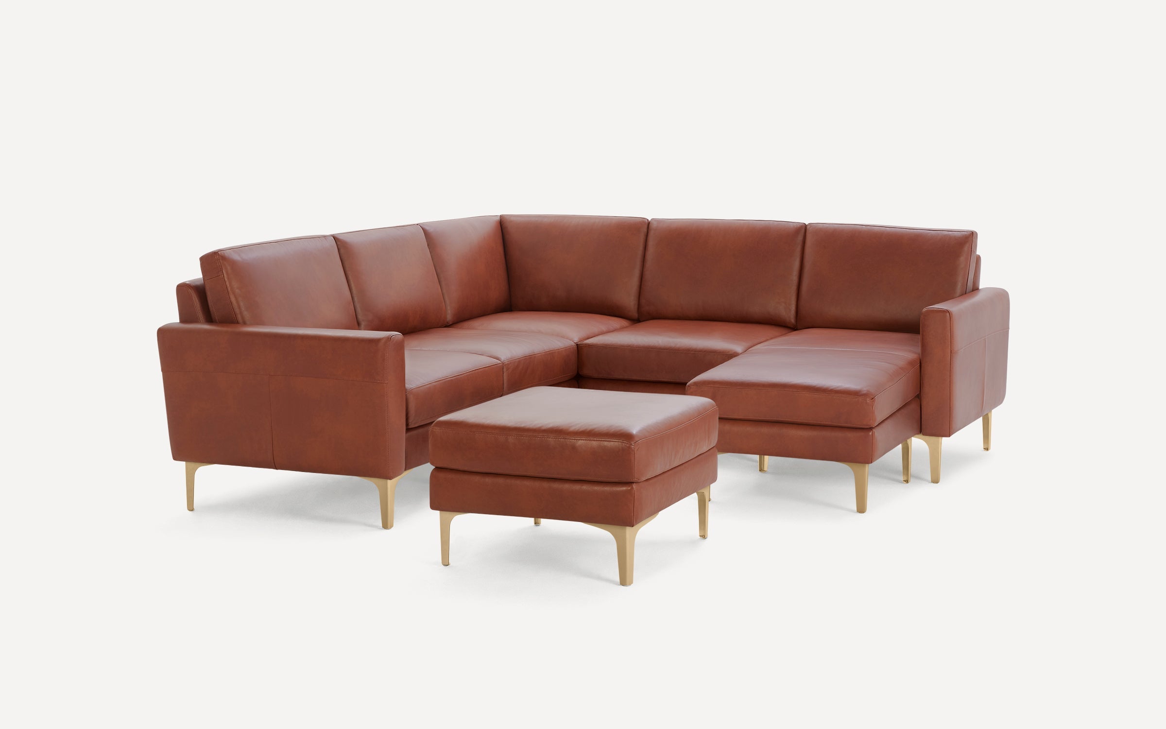Brown leather sectional sofa with gold metal legs and matching ottoman on a white background.