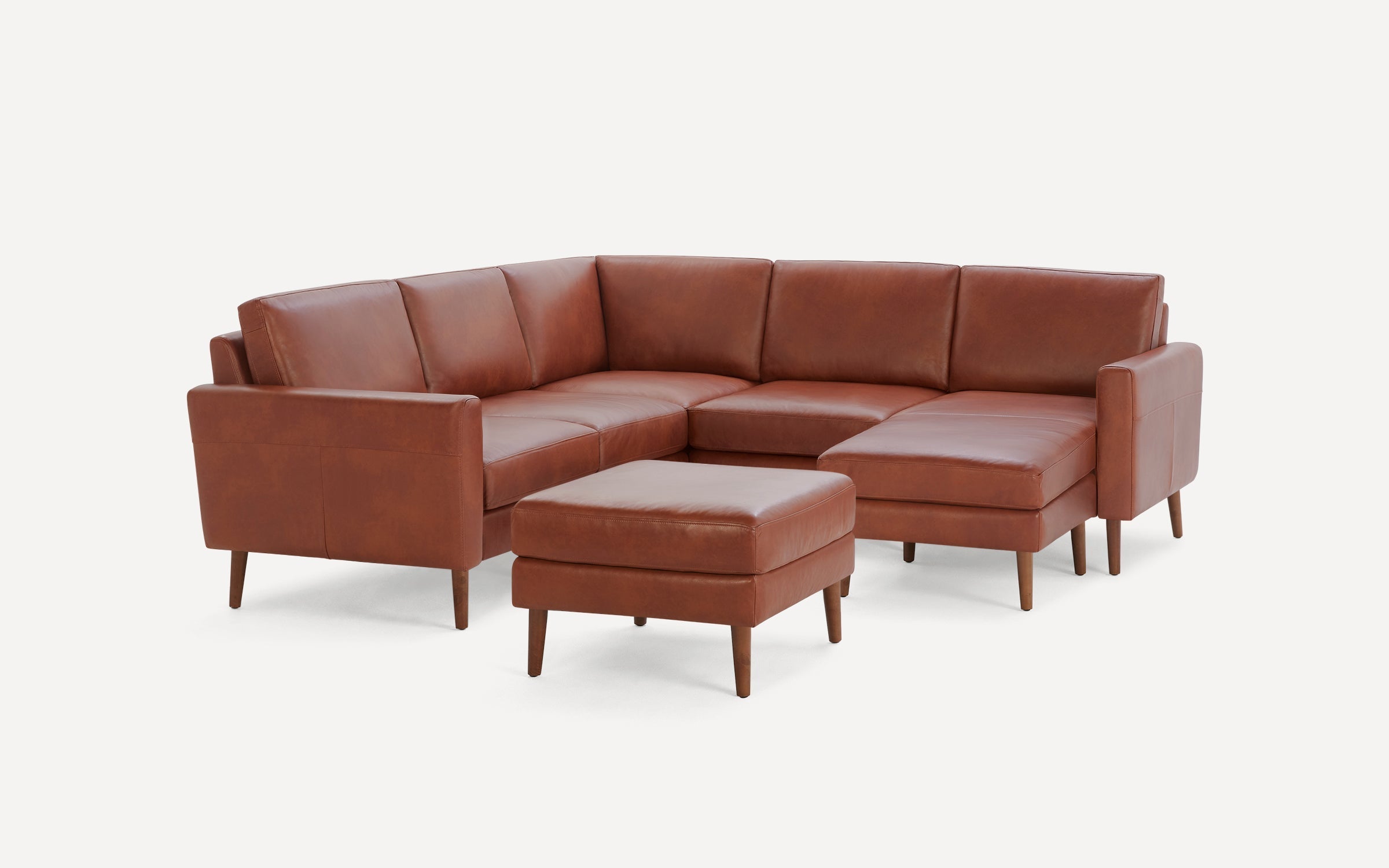 Brown leather mid-century modern sectional sofa with matching ottoman, tapered wooden legs, and clean lines.
