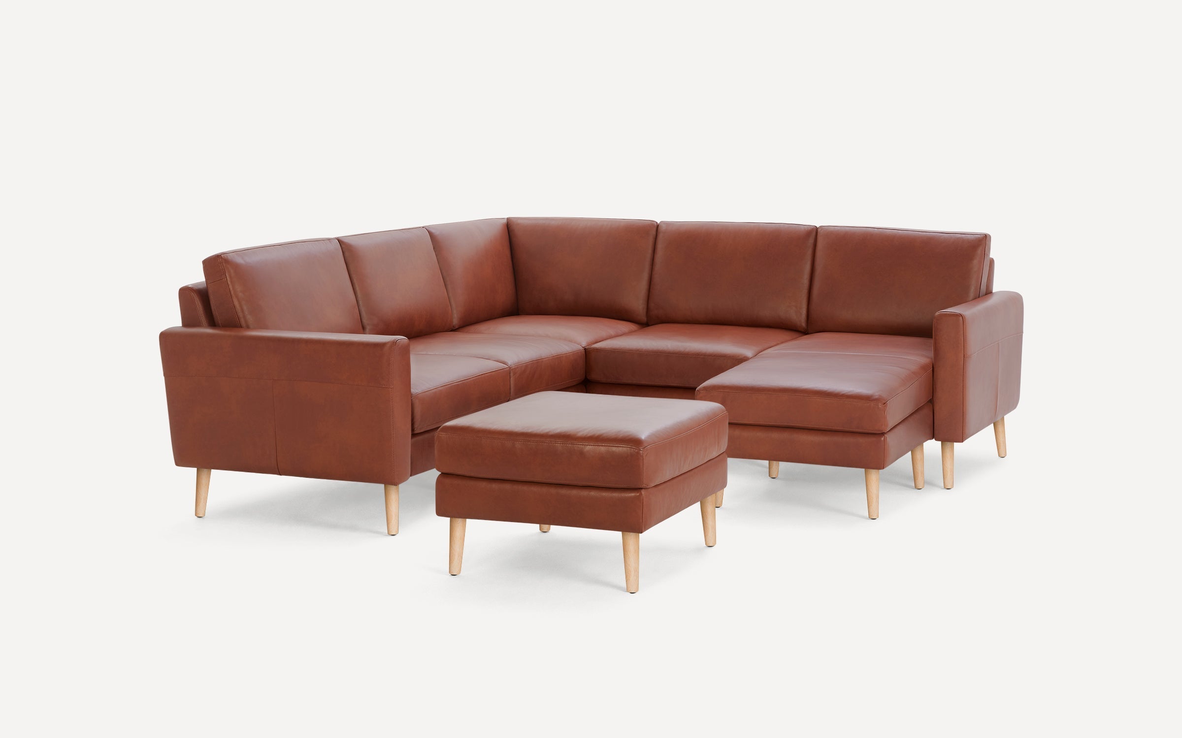 Brown leather L-shaped sectional sofa with wooden legs and matching leather ottoman against a white background.
