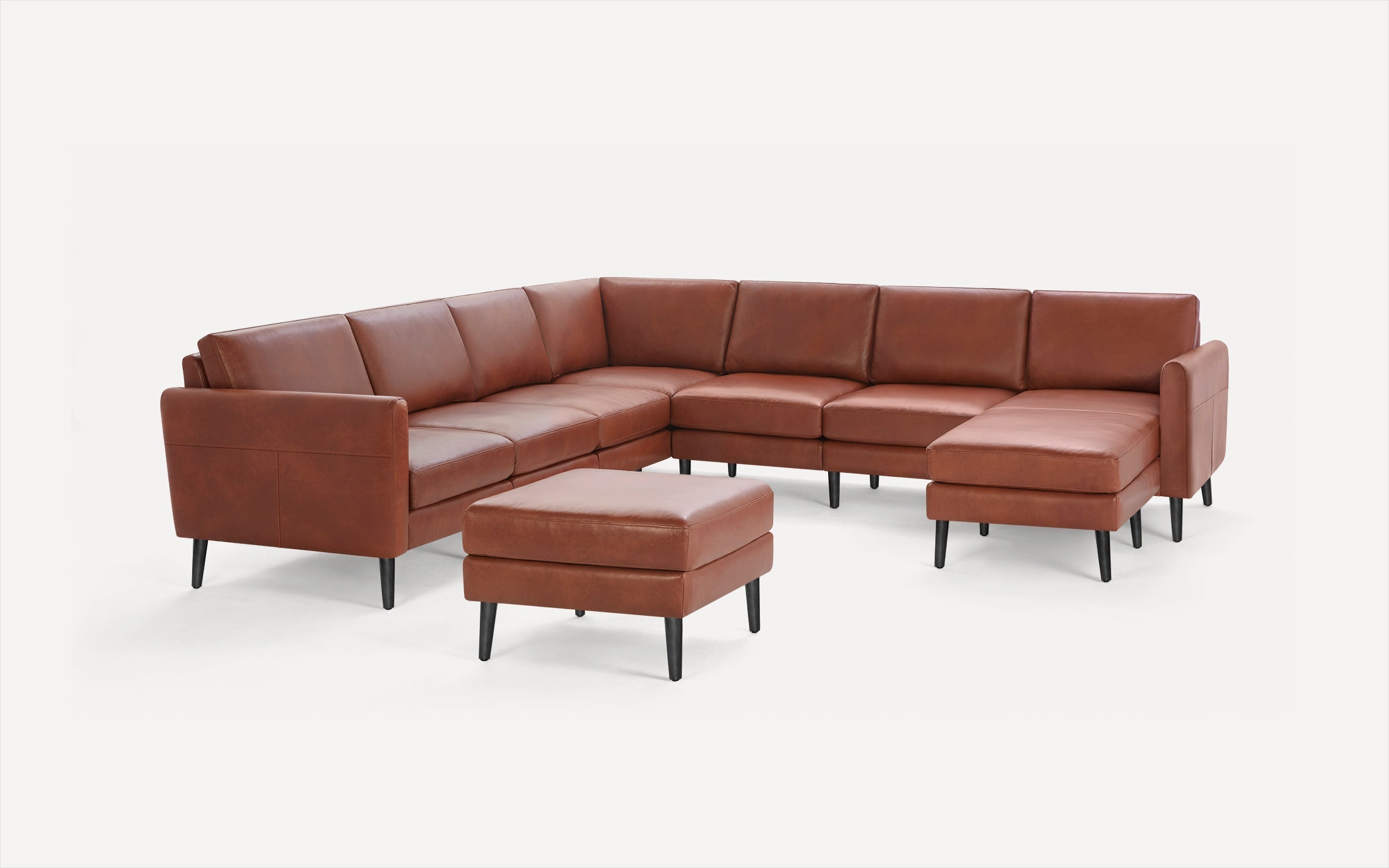 Brown leather L-shaped sectional sofa with matching ottoman, supported by black tapered legs on white background.