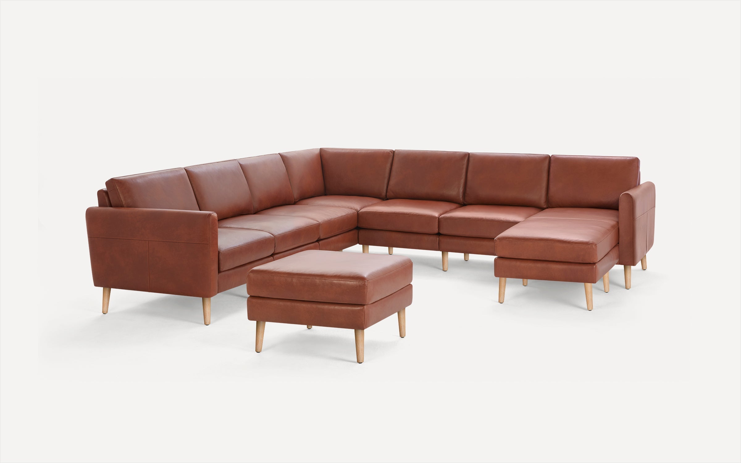 Brown leather sectional sofa with wooden legs accompanied by a matching ottoman on a white background.