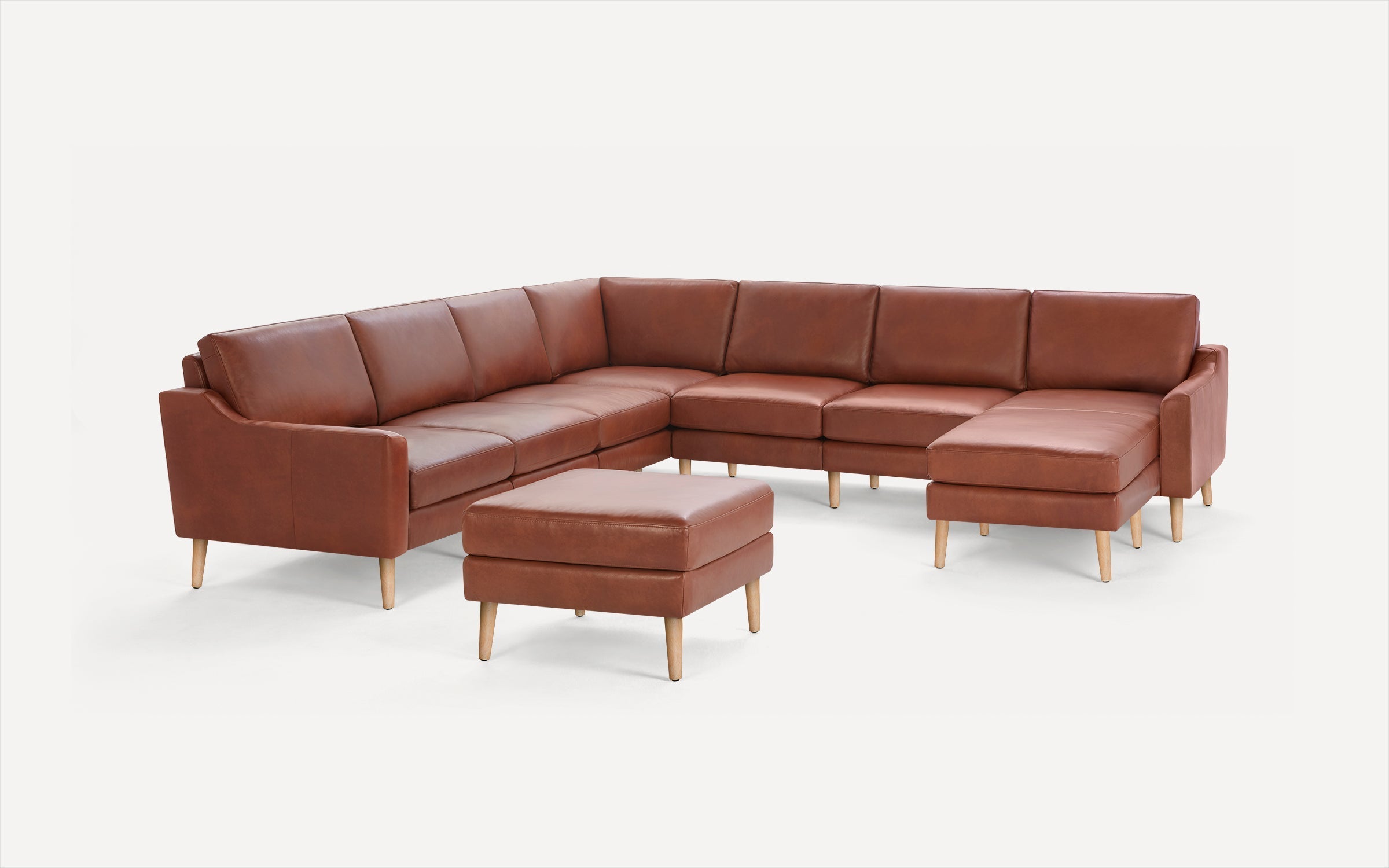 Brown leather sectional sofa with wooden legs and a matching ottoman on a white background.
