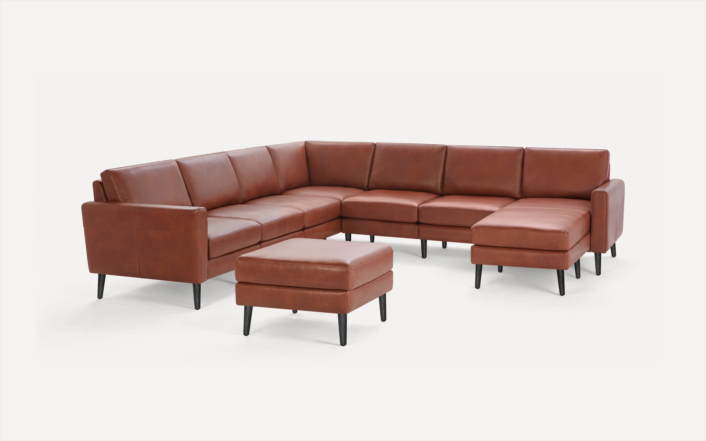 Brown leather L-shaped sectional sofa with black tapered legs and matching square ottoman on a white background.