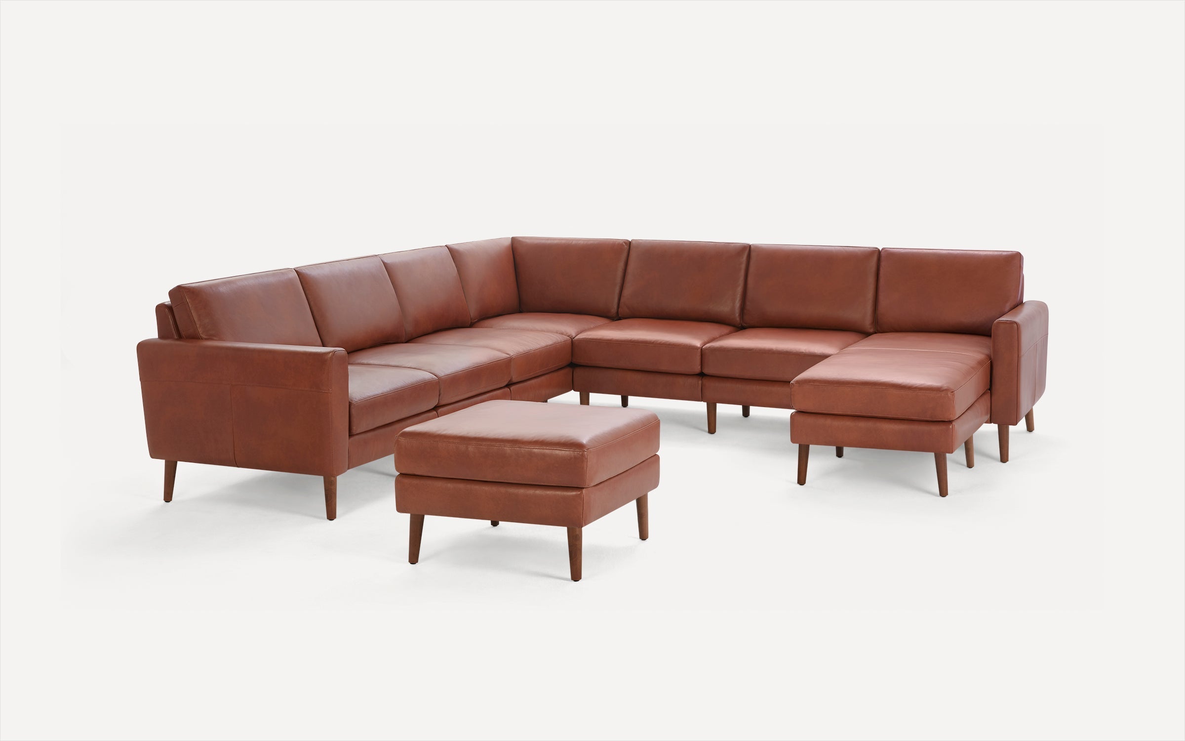 Brown leather mid-century modern sectional sofa with matching ottoman, wooden legs, and clean lines on a white background.