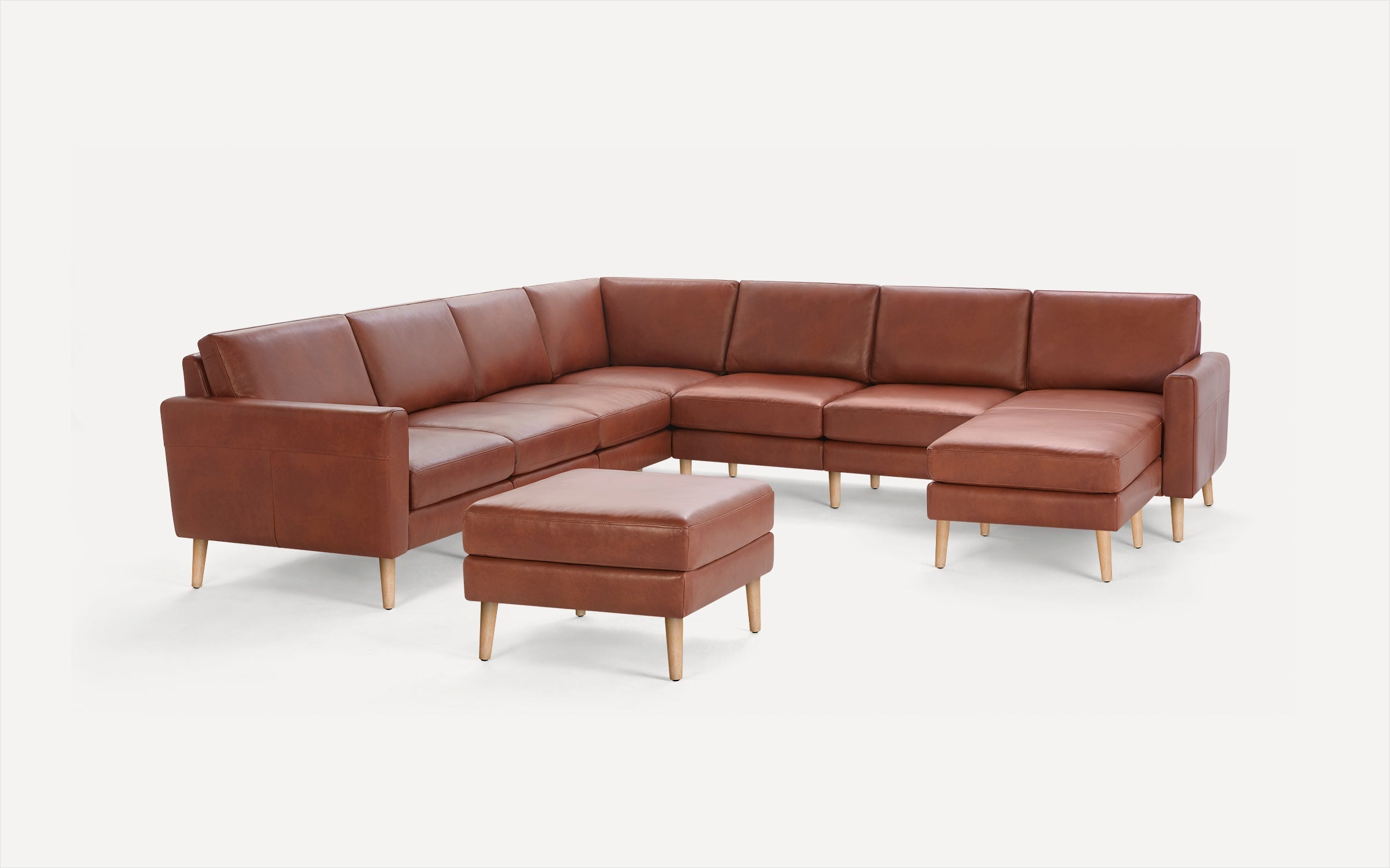Brown leather L-shaped sectional sofa with wooden legs and matching square ottoman on a white background.