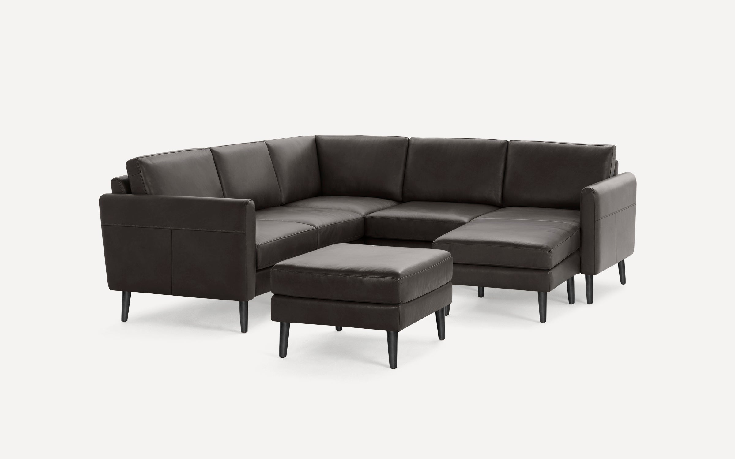 Dark brown leather sectional sofa with chaise lounge and matching ottoman, featuring sleek black legs and modern design.
